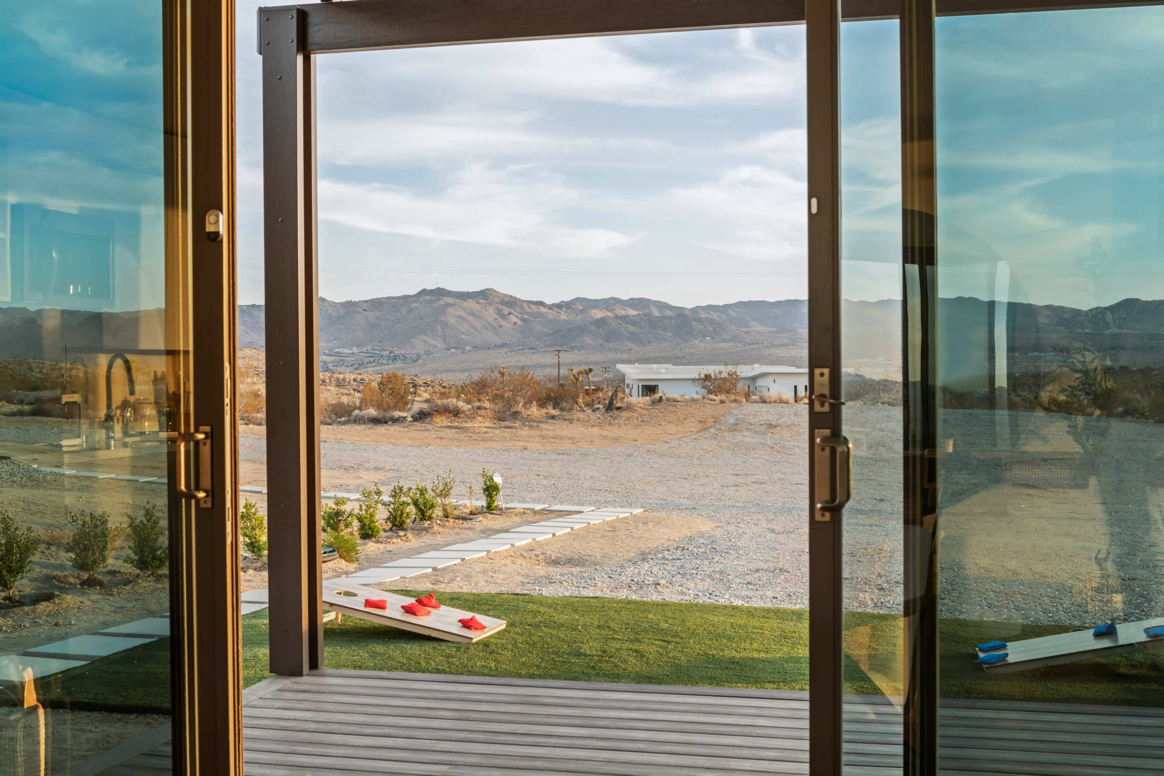 The image shows an interior view looking out through sliding glass doors towards a desert landscape with mountains and a lake in the distance.