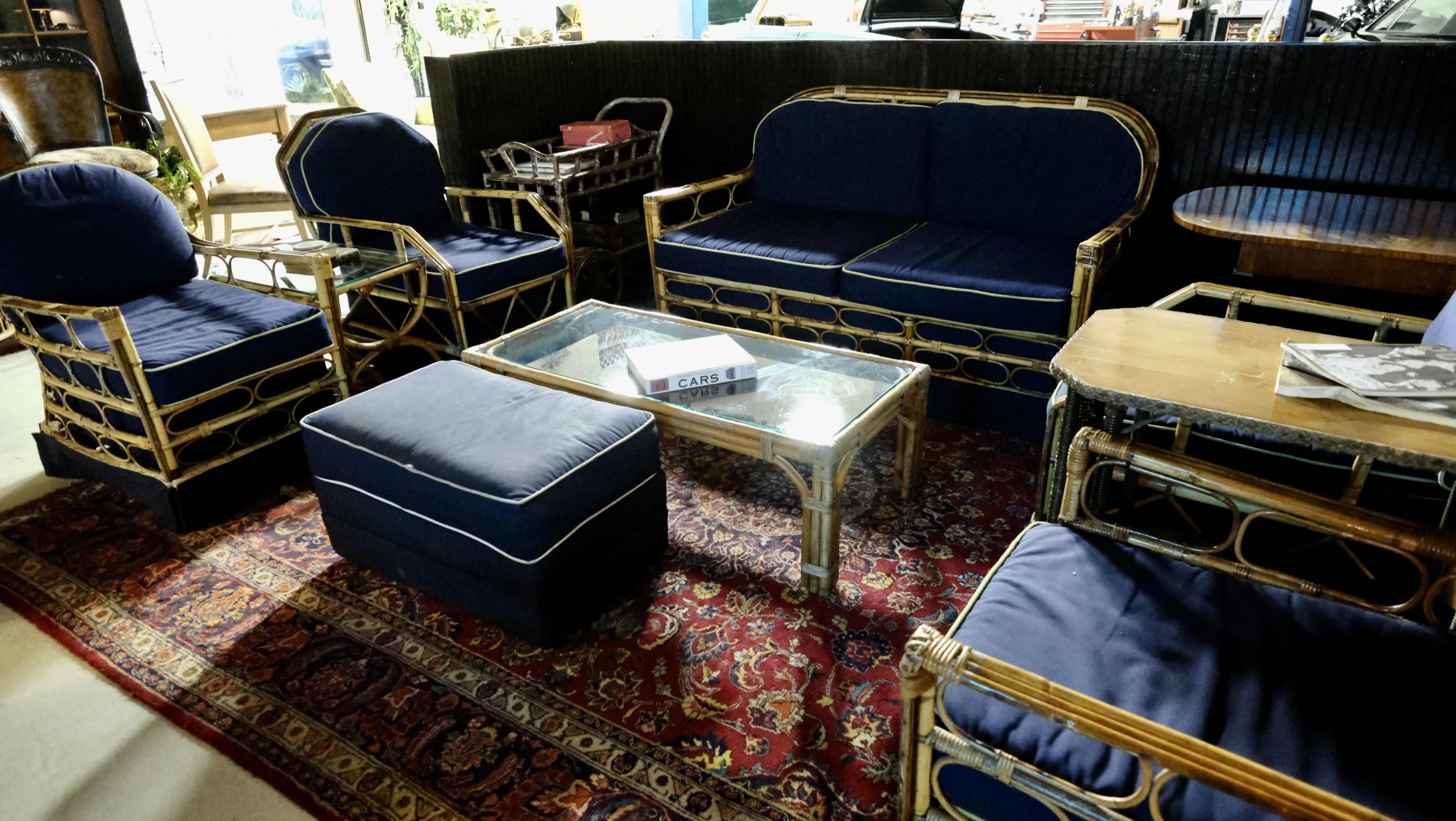 A seating area featuring a blue upholstered sofa set with gold-toned metal frames, a glass coffee table, and a patterned area rug.