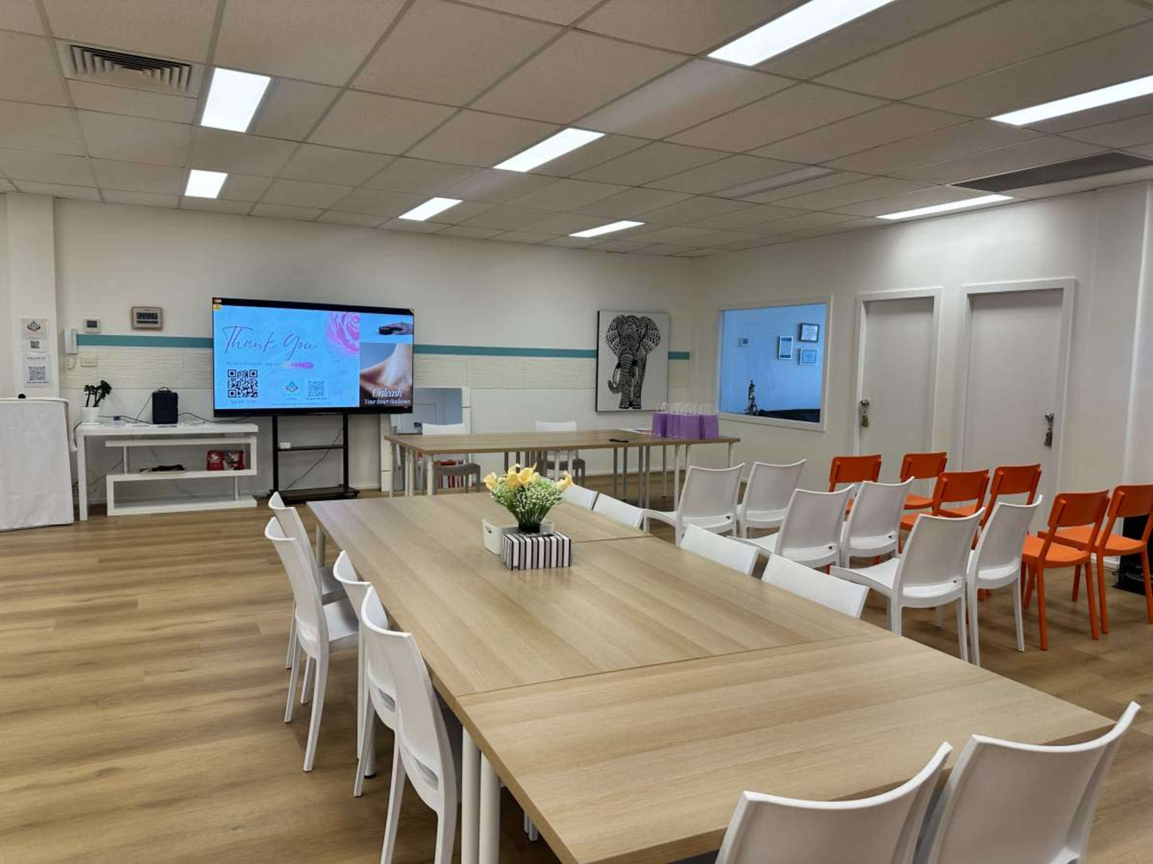 The image shows a modern conference room with a large table, several chairs, and multiple screens displaying information on the walls.