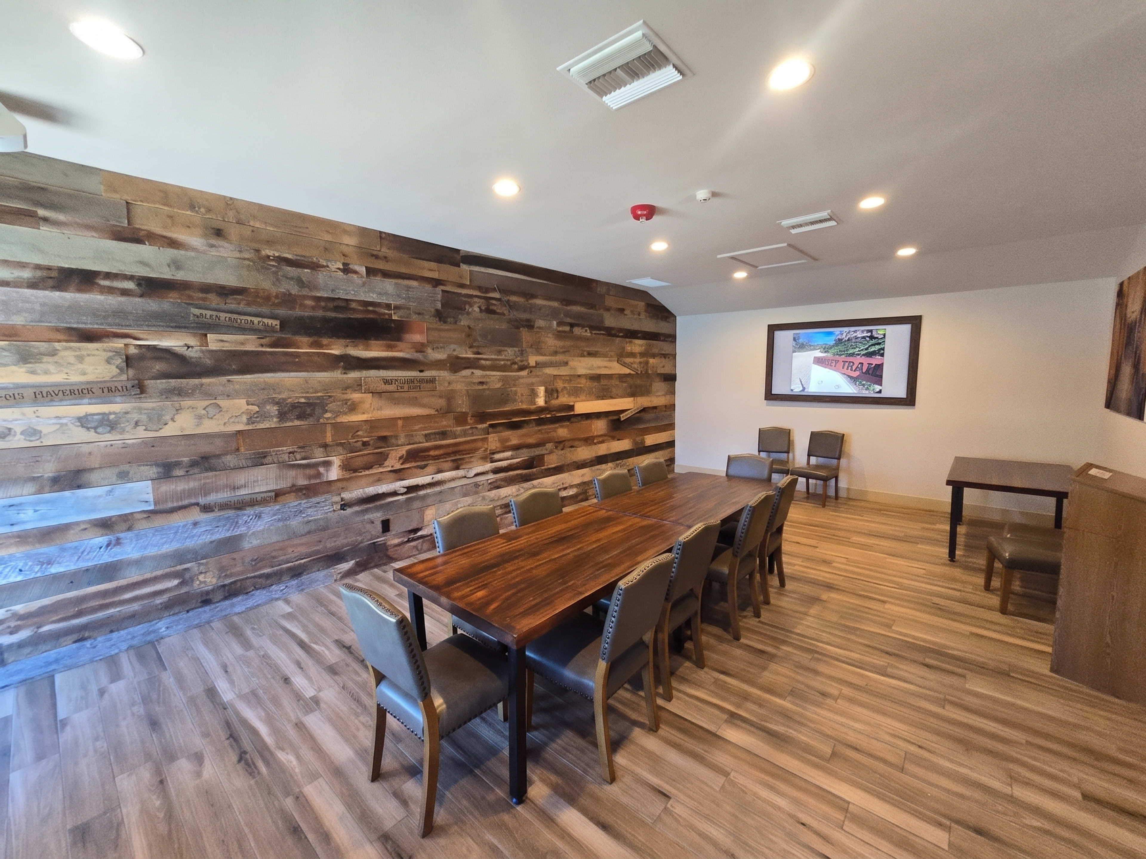 The image shows a spacious dining room with a long wooden table surrounded by chairs, and a wall made of rustic wooden planks.