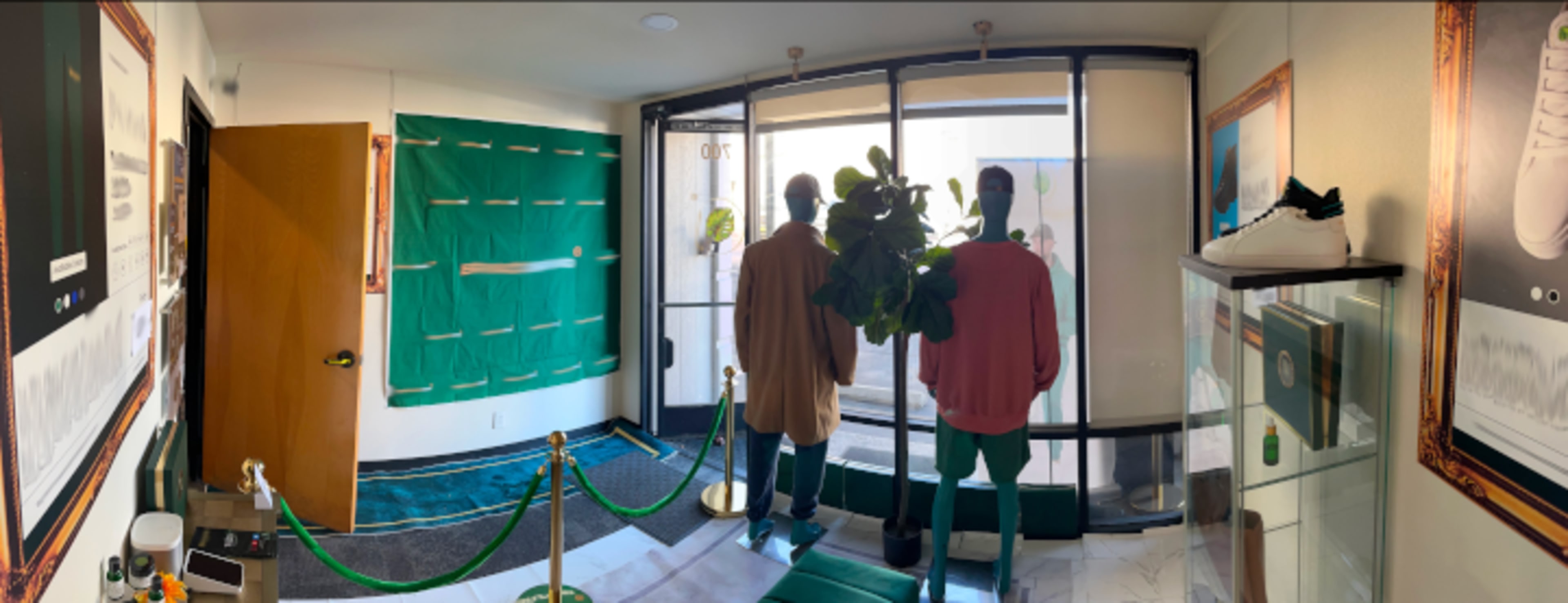 The image shows the interior of a storefront featuring two mannequin figures dressed in casual attire, with a glass display showcasing products and a green rope barrier.