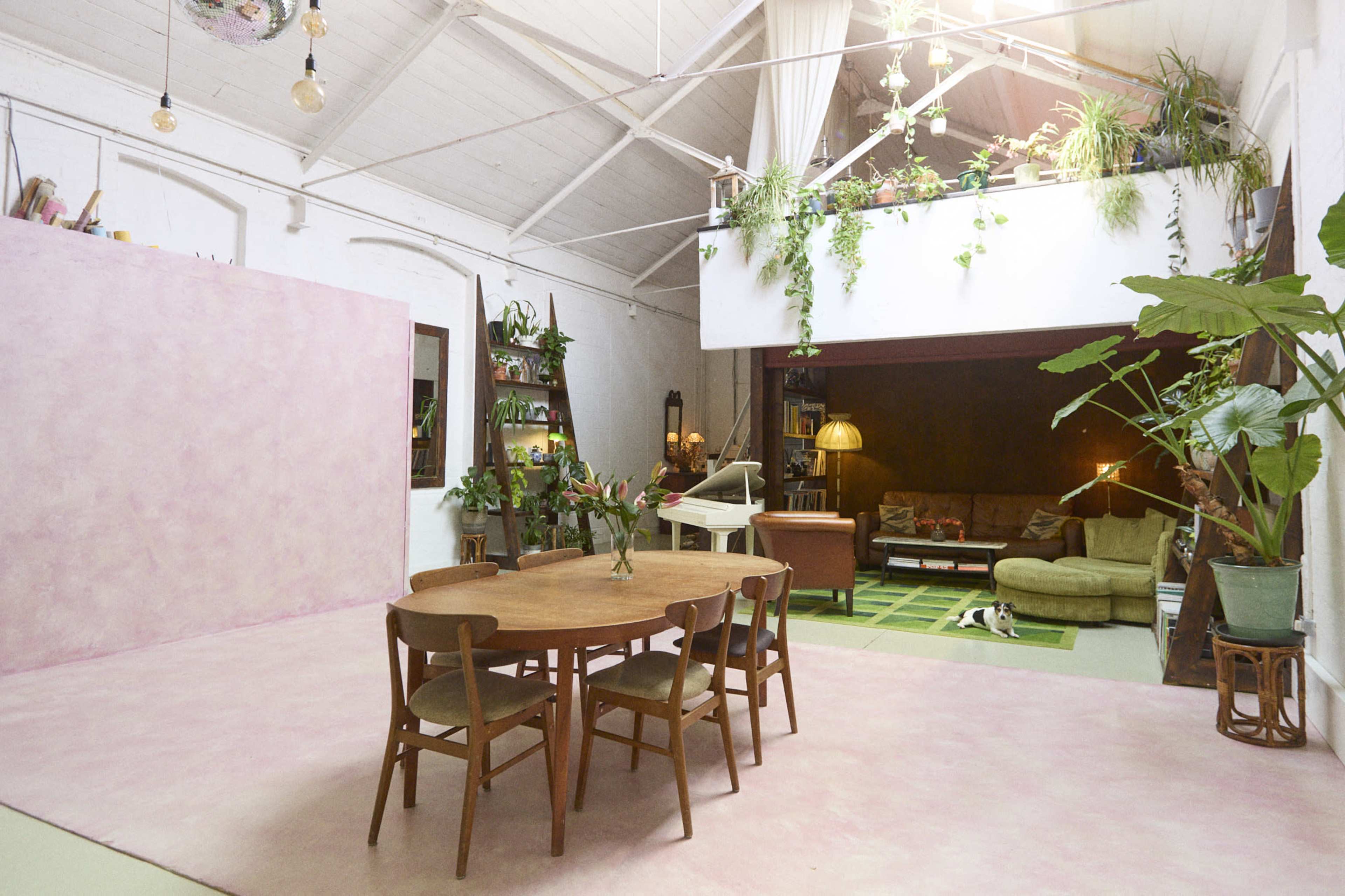 A spacious interior with a pink floor, a wooden dining table with chairs, and a second level featuring plants and a cozy seating area.