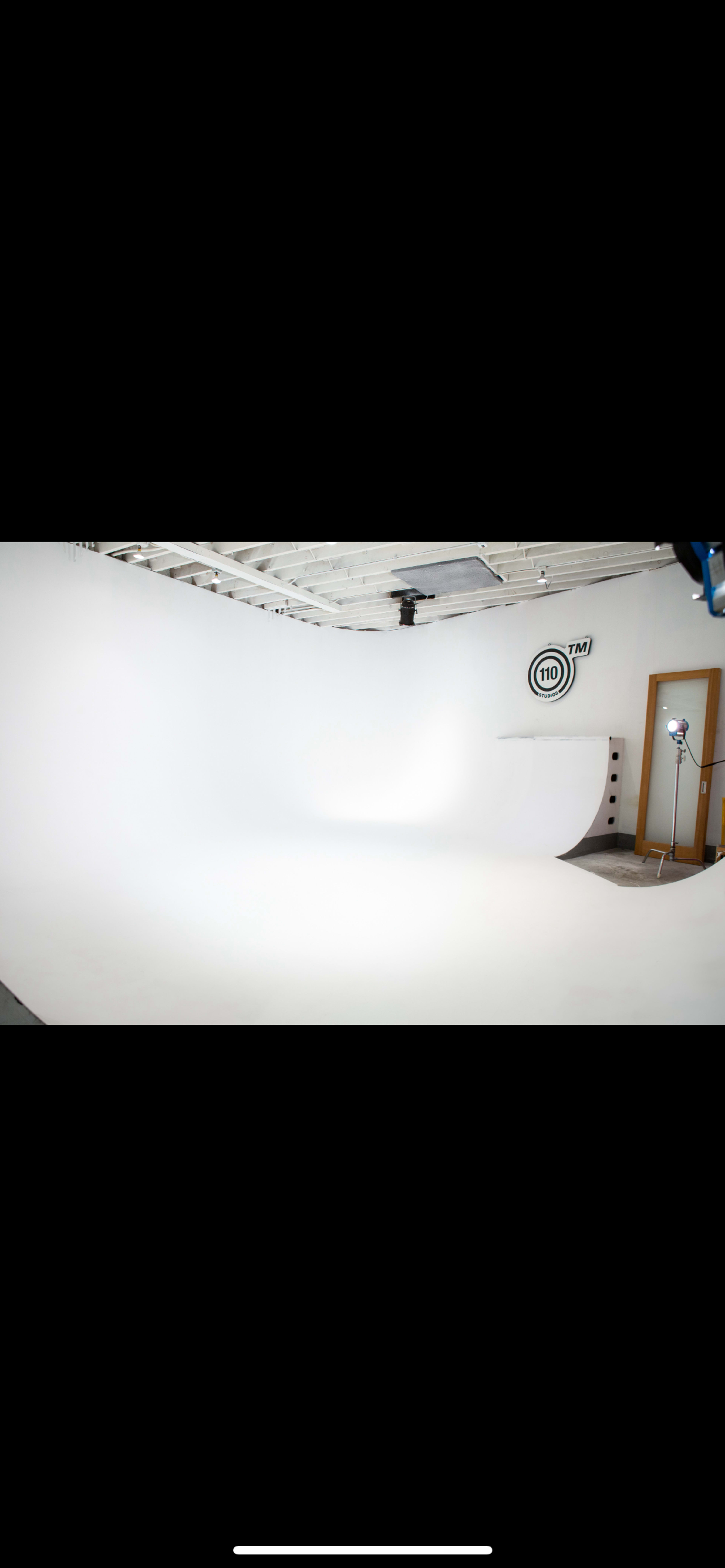 The image shows a minimalistic studio space with a white curved background, soft lighting, and equipment setup.