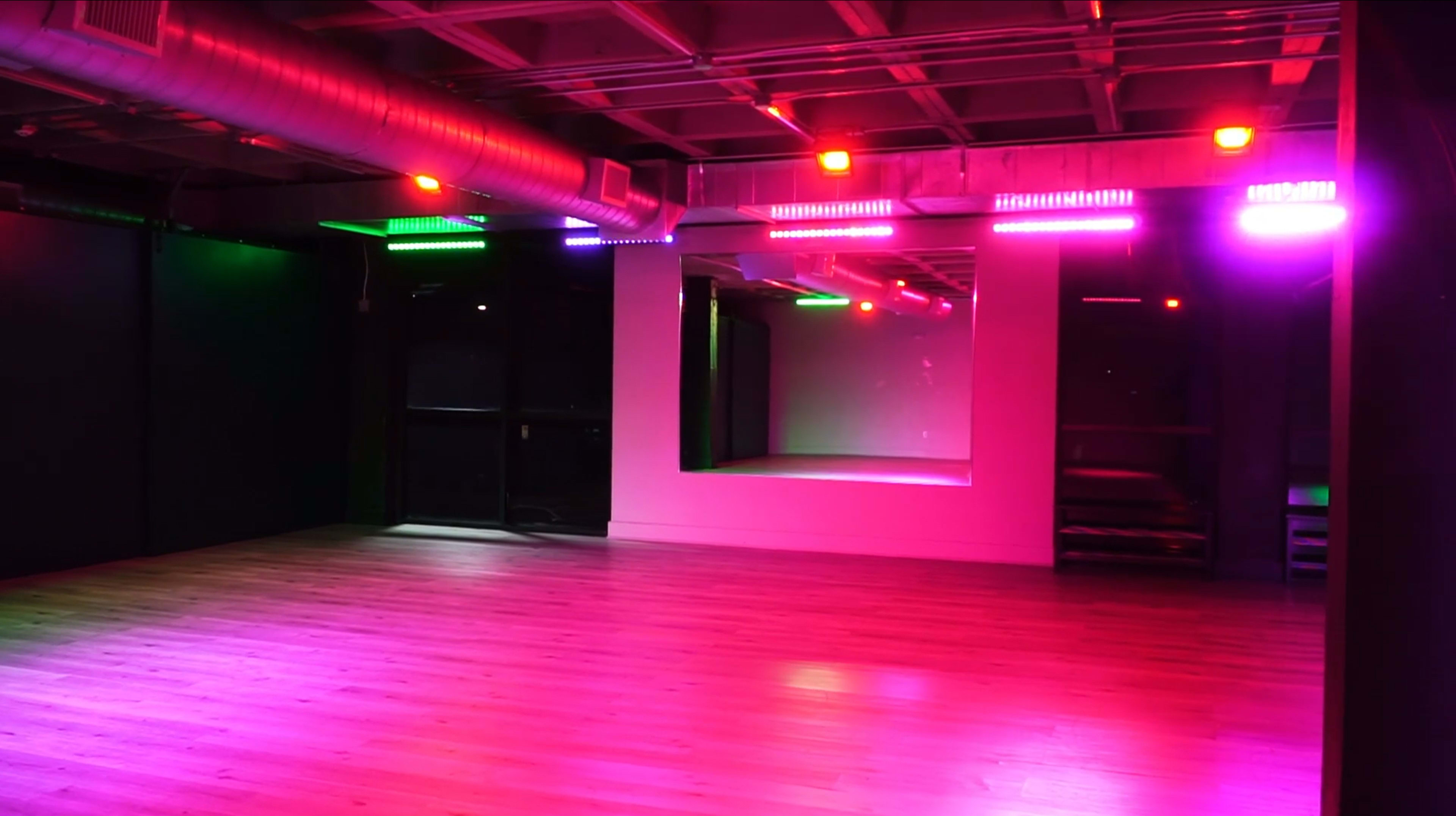 An empty dance studio with colorful LED lights illuminating the space and a large mirror on one wall.