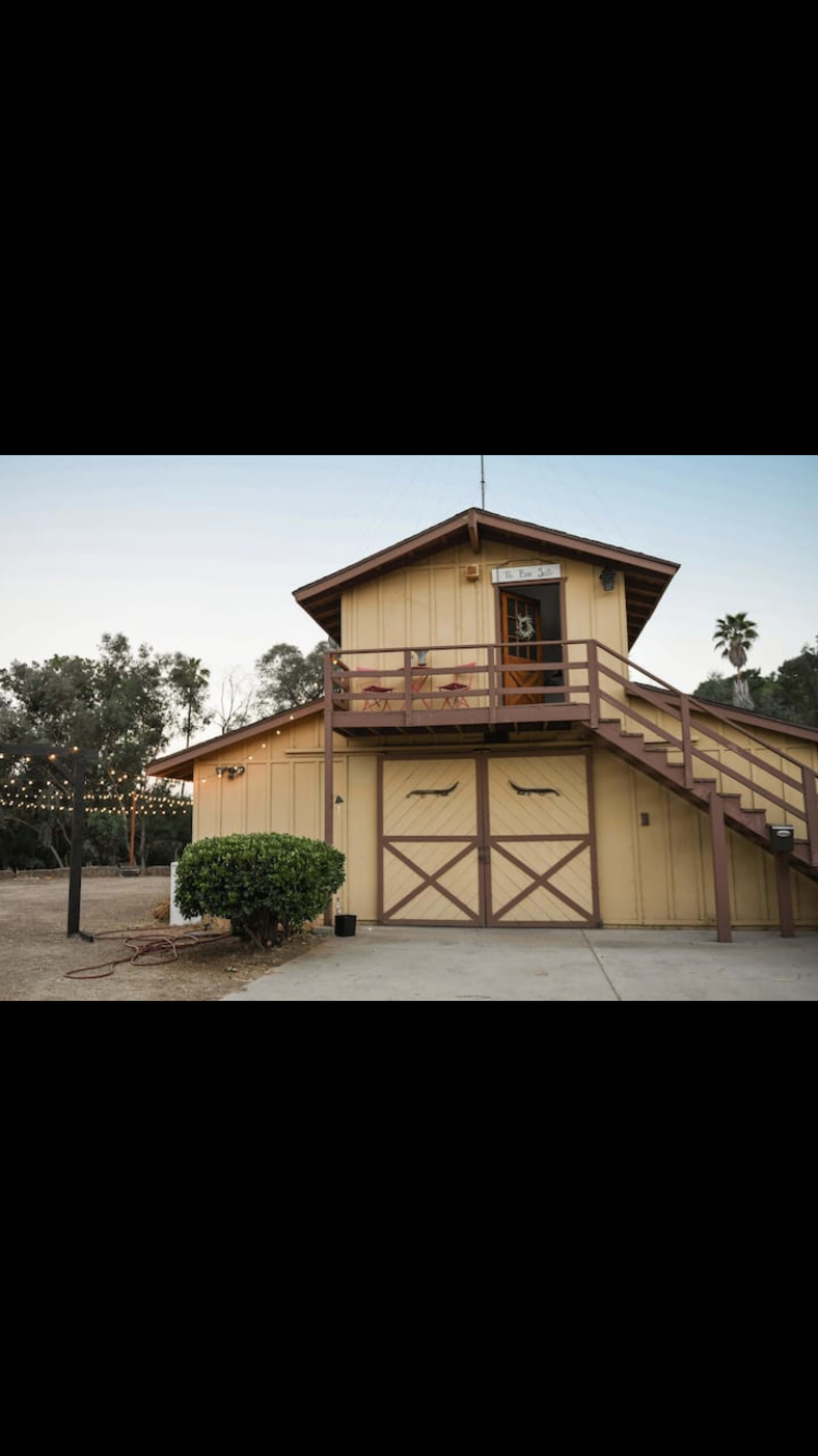 A two-story wooden building with a staircase leading to a second-floor entrance, surrounded by trees and outdoor lighting.
