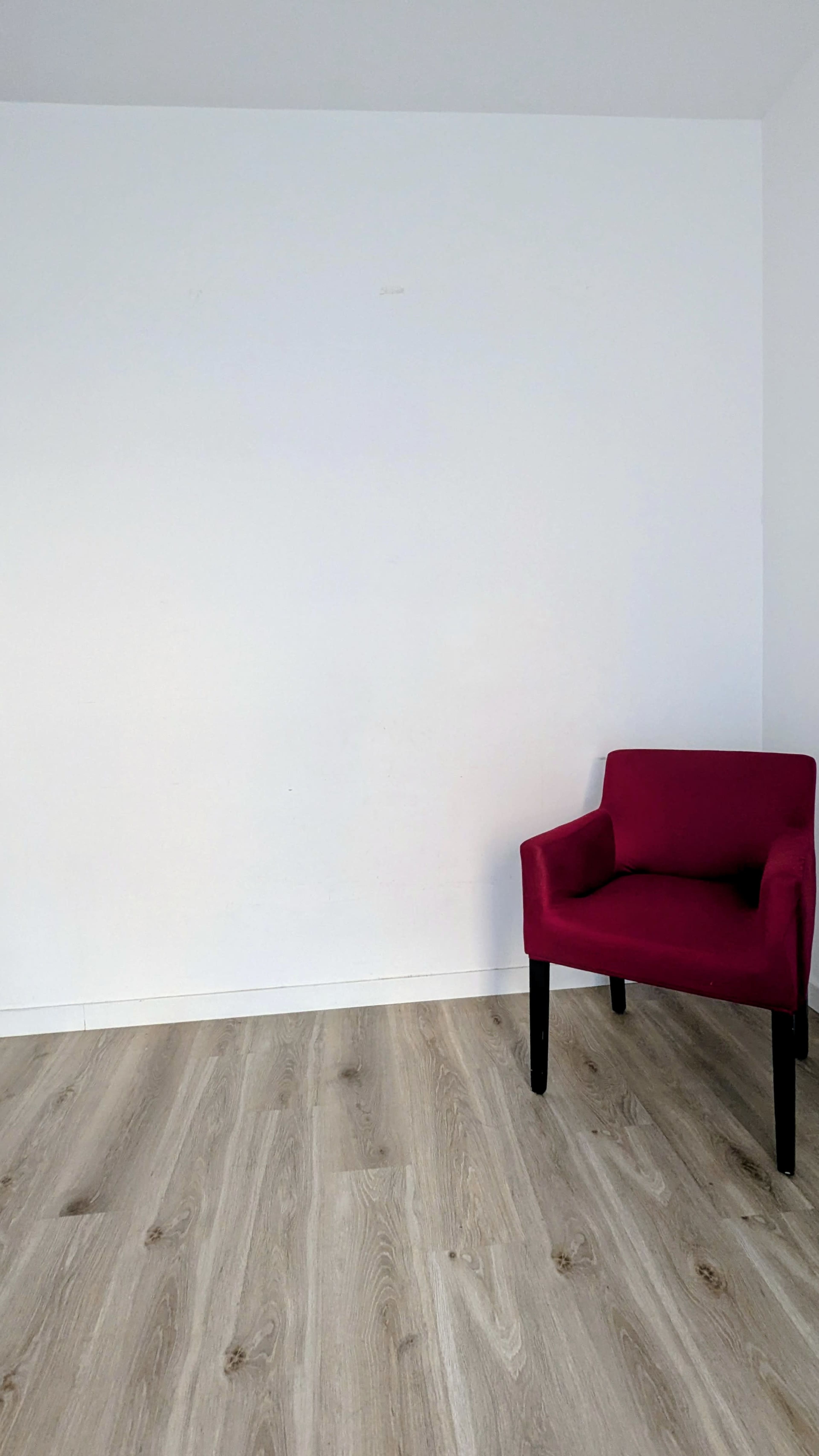 A single magenta chair sits on light wooden flooring in an empty room with a blank white wall.