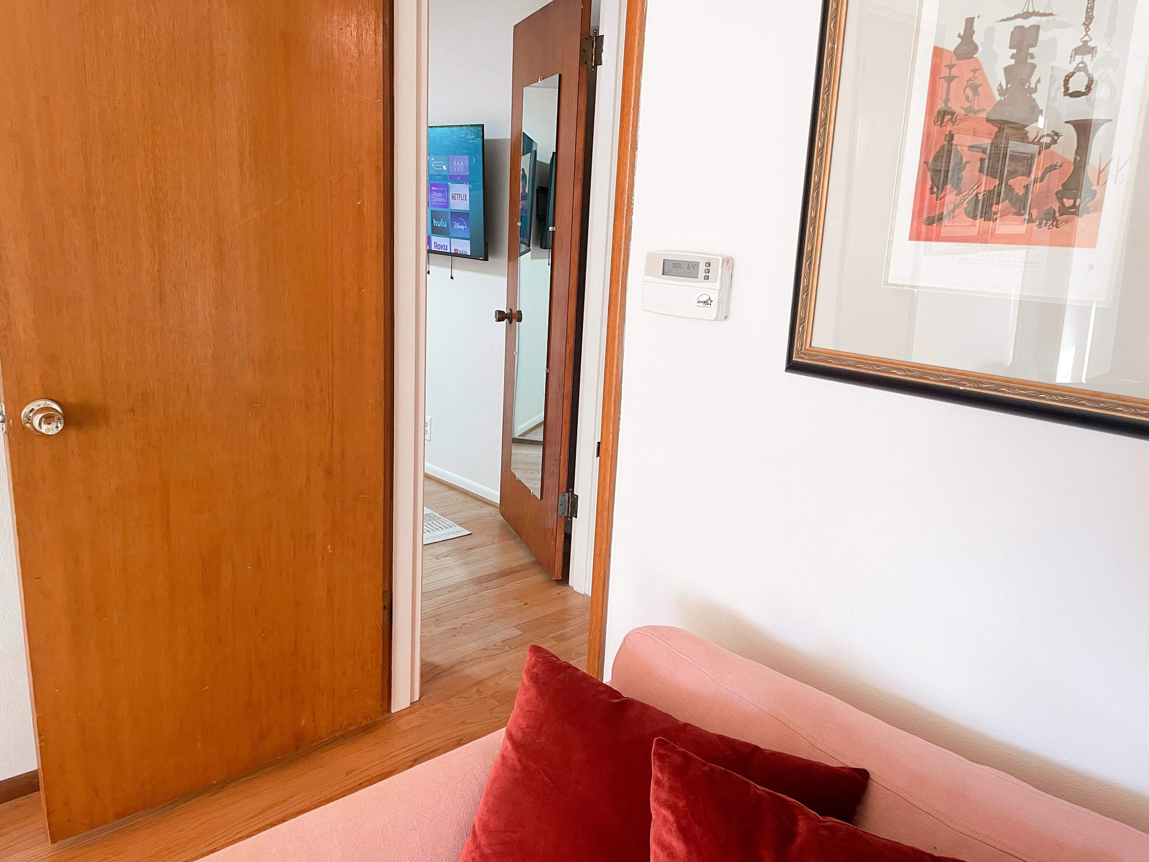 A living room with a pink sofa, a closed wooden door, and a glimpse of a hallway and a mirrored door leading to another room.
