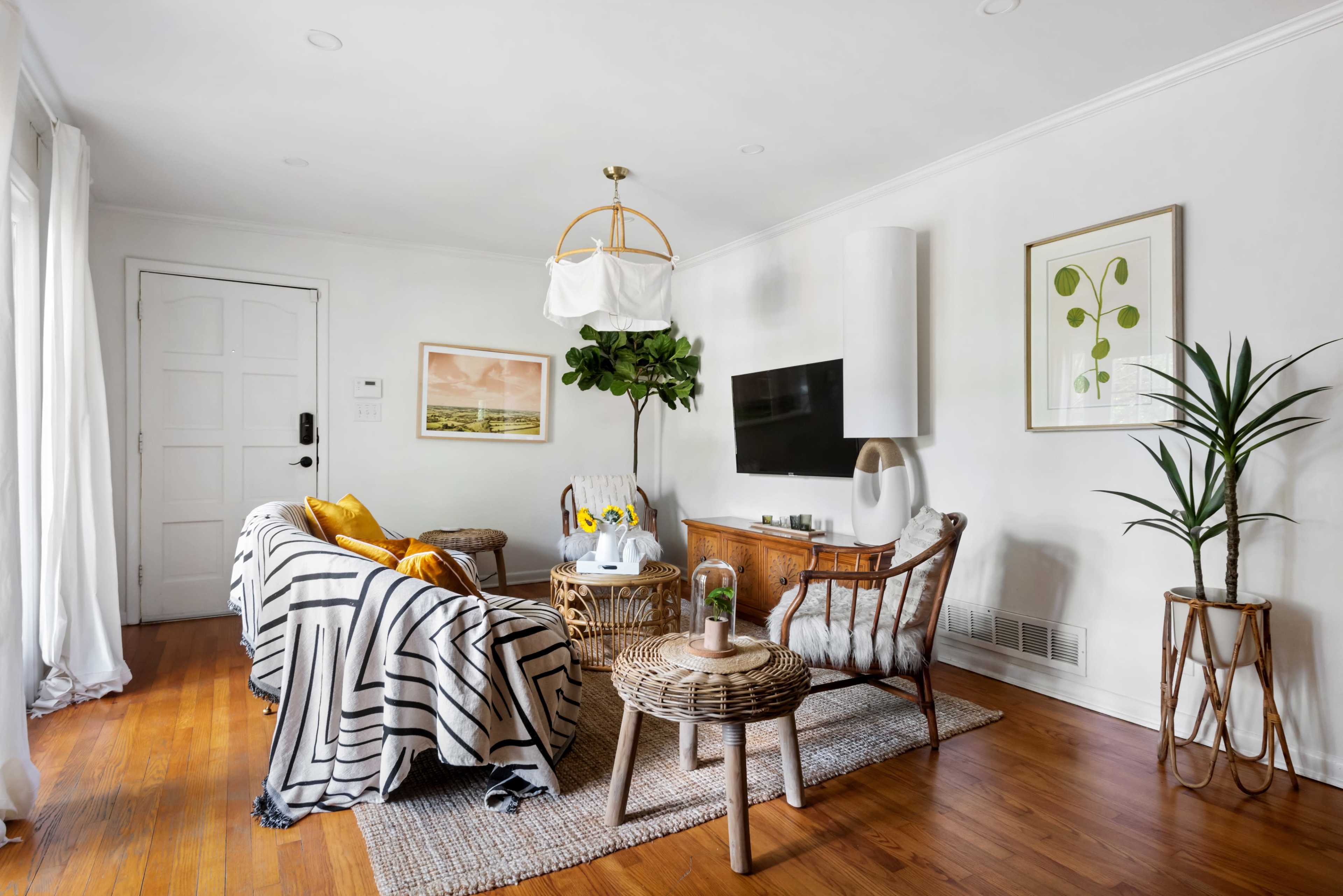The image shows a cozy living room with a striped sofa, a small coffee table, a potted plant, and a television on a wooden cabinet.