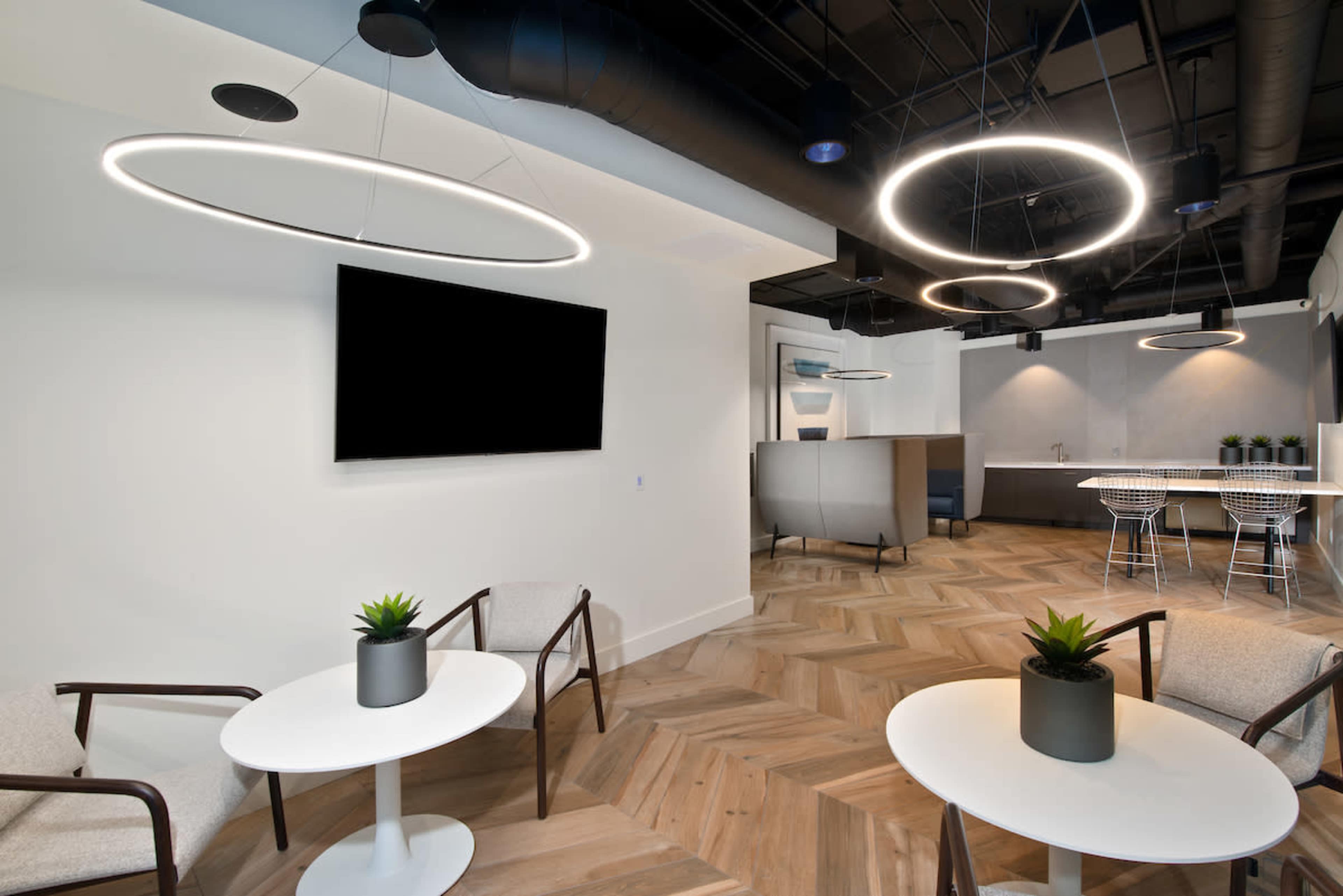 The image shows a modern interior space with two circular light fixtures, light wood flooring, and a seating area that includes two small tables and chairs.