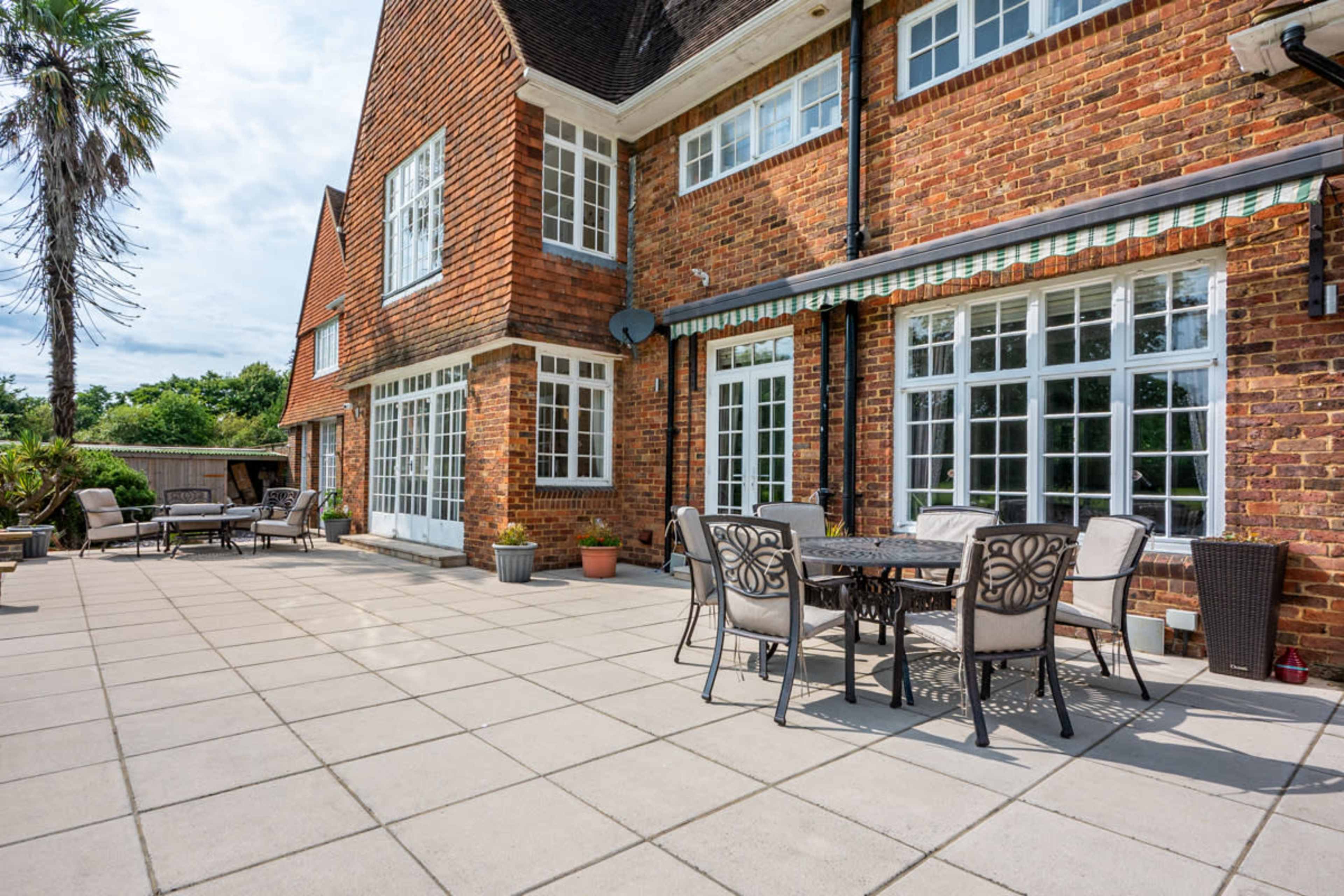 A brick house with large windows and a spacious patio area furnished with tables and chairs.