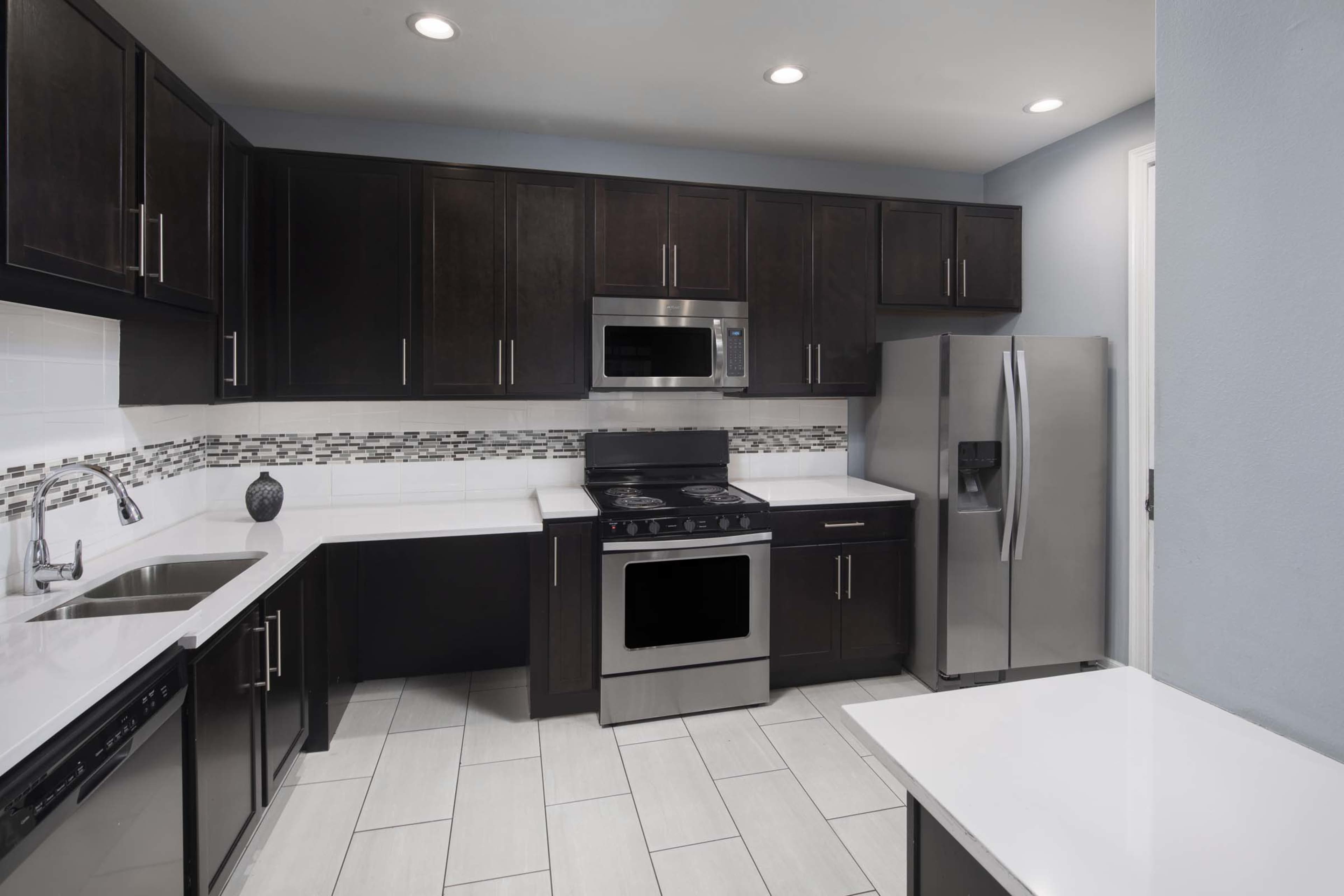 The image shows a modern kitchen with dark cabinetry, stainless steel appliances, and tiled flooring.