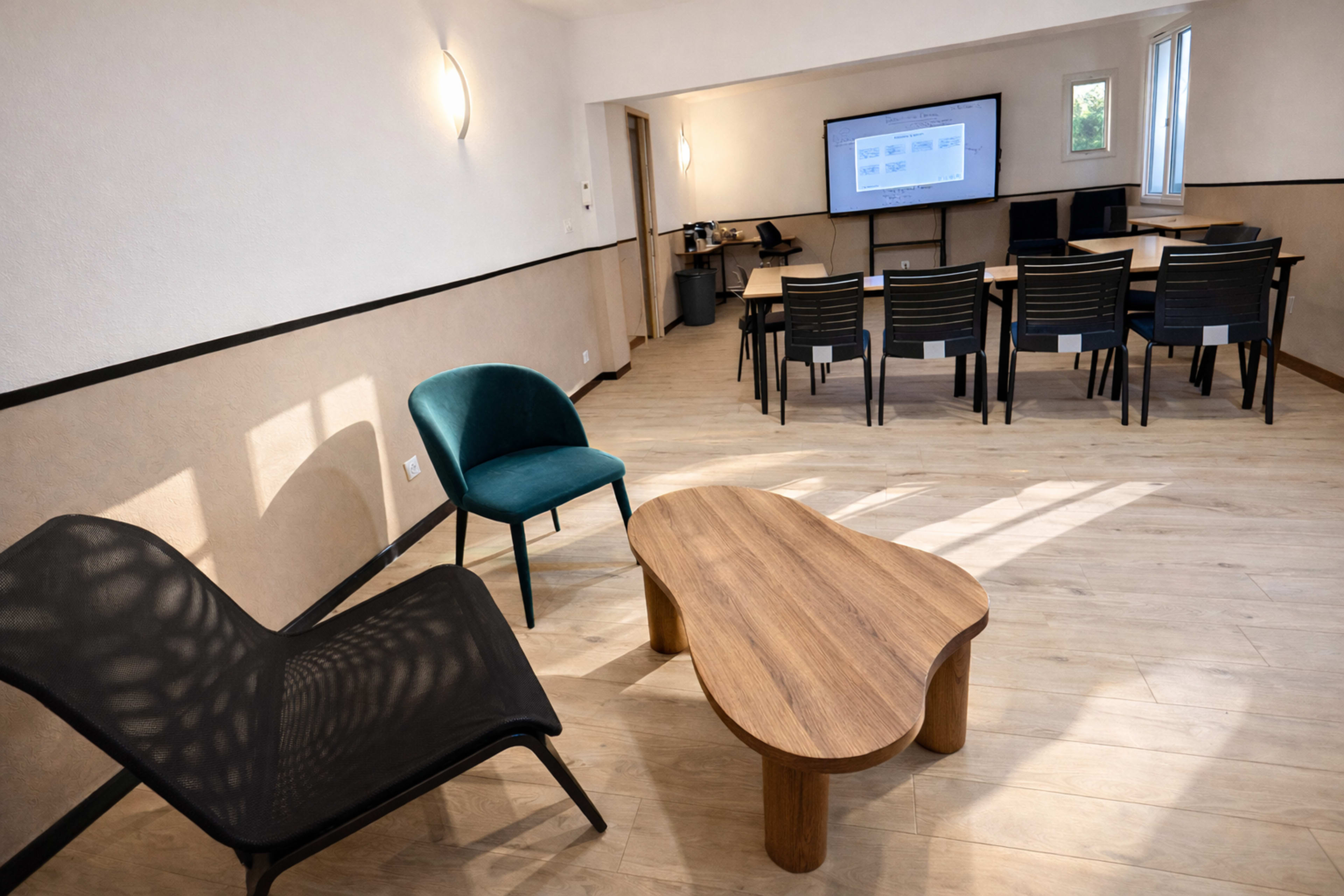 The image shows a modern meeting room with a large screen, a rectangular table surrounded by chairs, and two seating options in a corner.