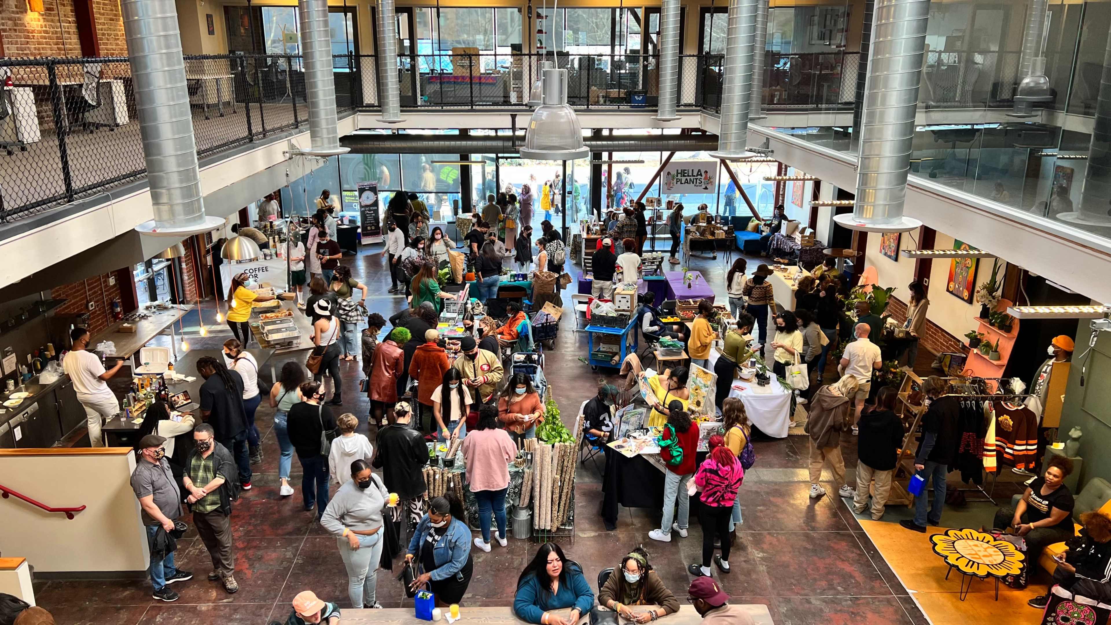 A bustling indoor market with numerous vendors and visitors engaging in various activities around a large, open space.