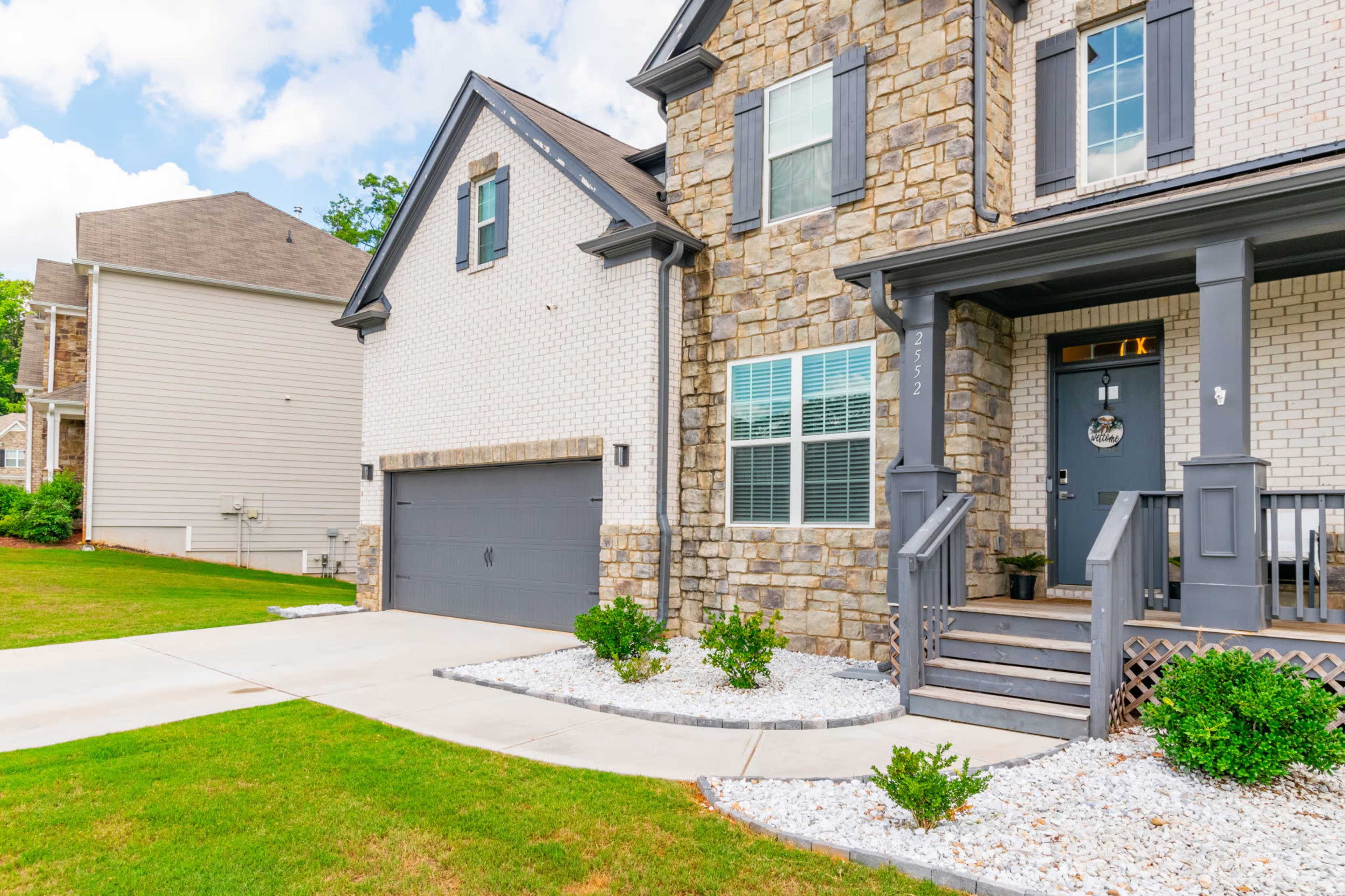 A house with a stone and brick exterior features a driveway, garage, and landscaped front yard.