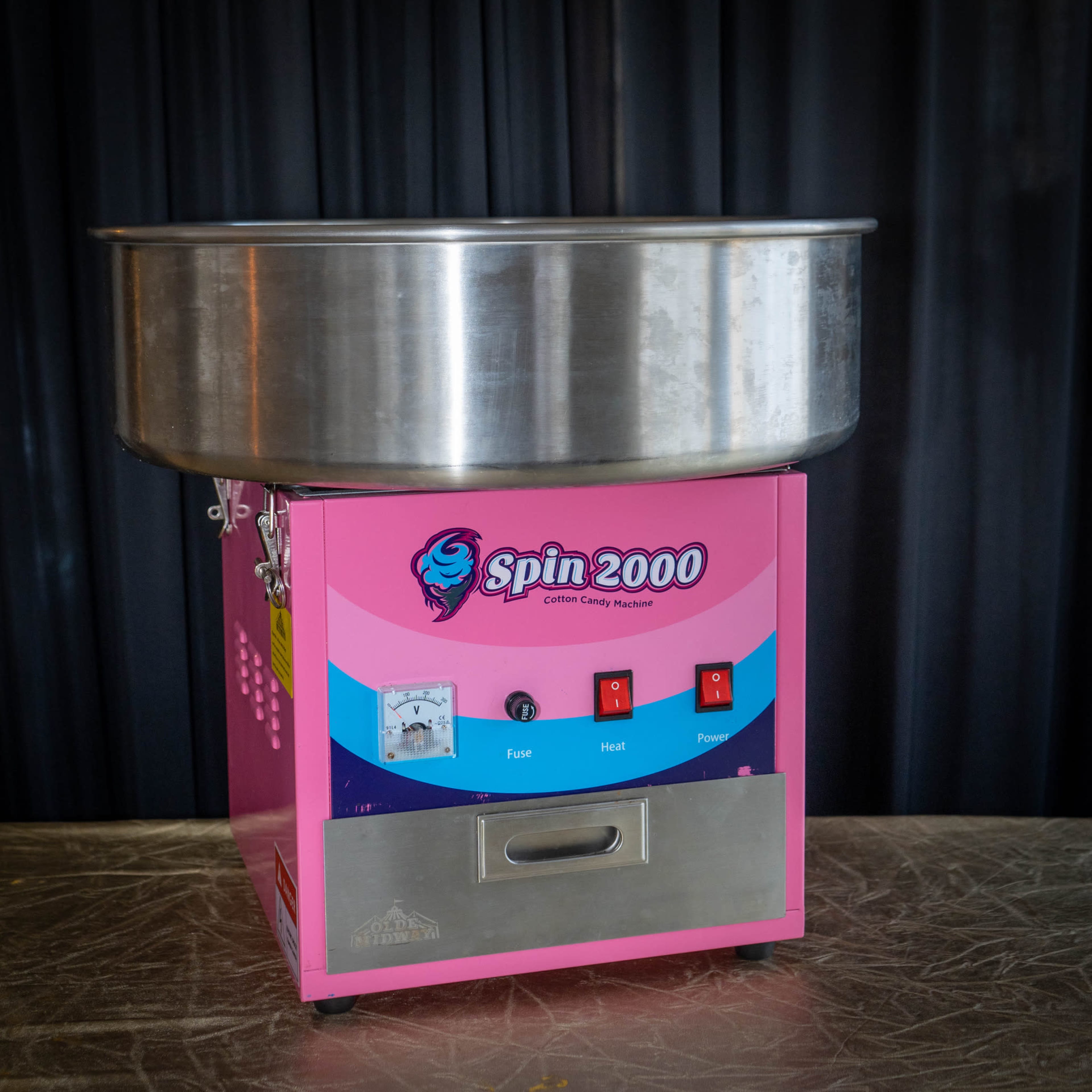 The image shows a pink and silver cotton candy machine with a large round bowl on top and control buttons on the front.