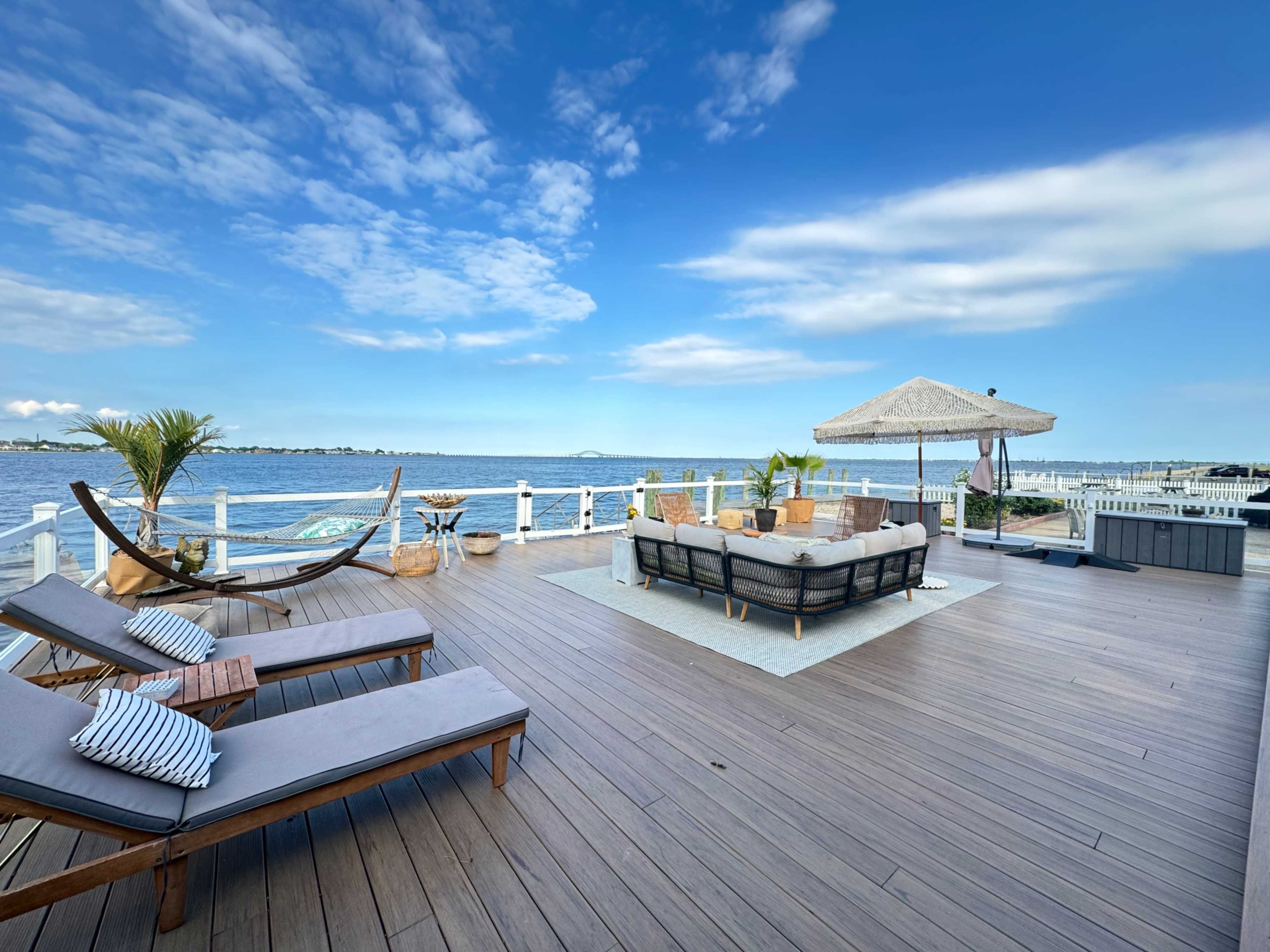 A tranquil outdoor deck overlooking a calm body of water, furnished with lounge chairs, a seating area, and a shaded gazebo.