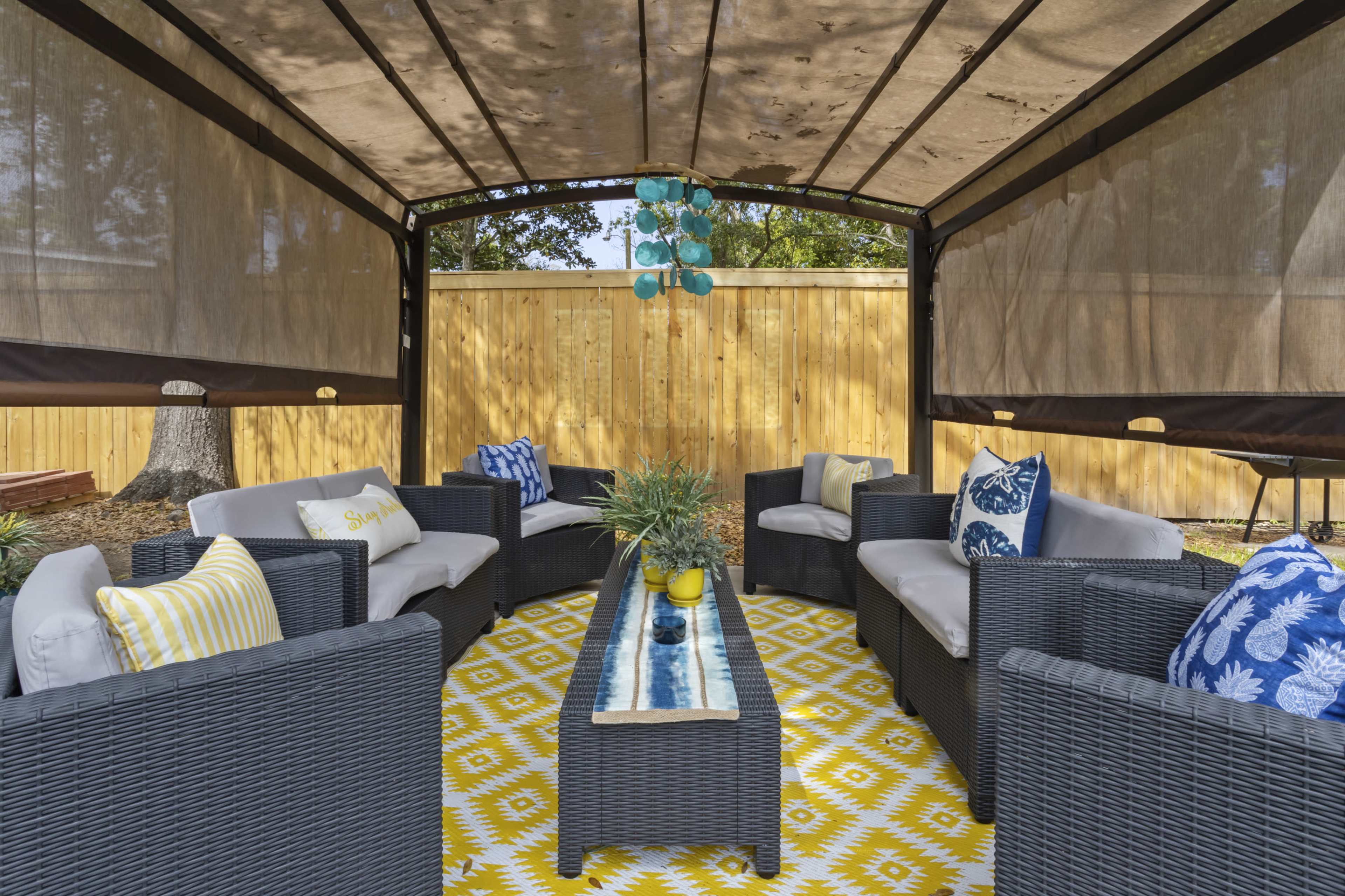 A cozy outdoor seating area features a rectangular table surrounded by gray and blue cushioned chairs under a canopy.