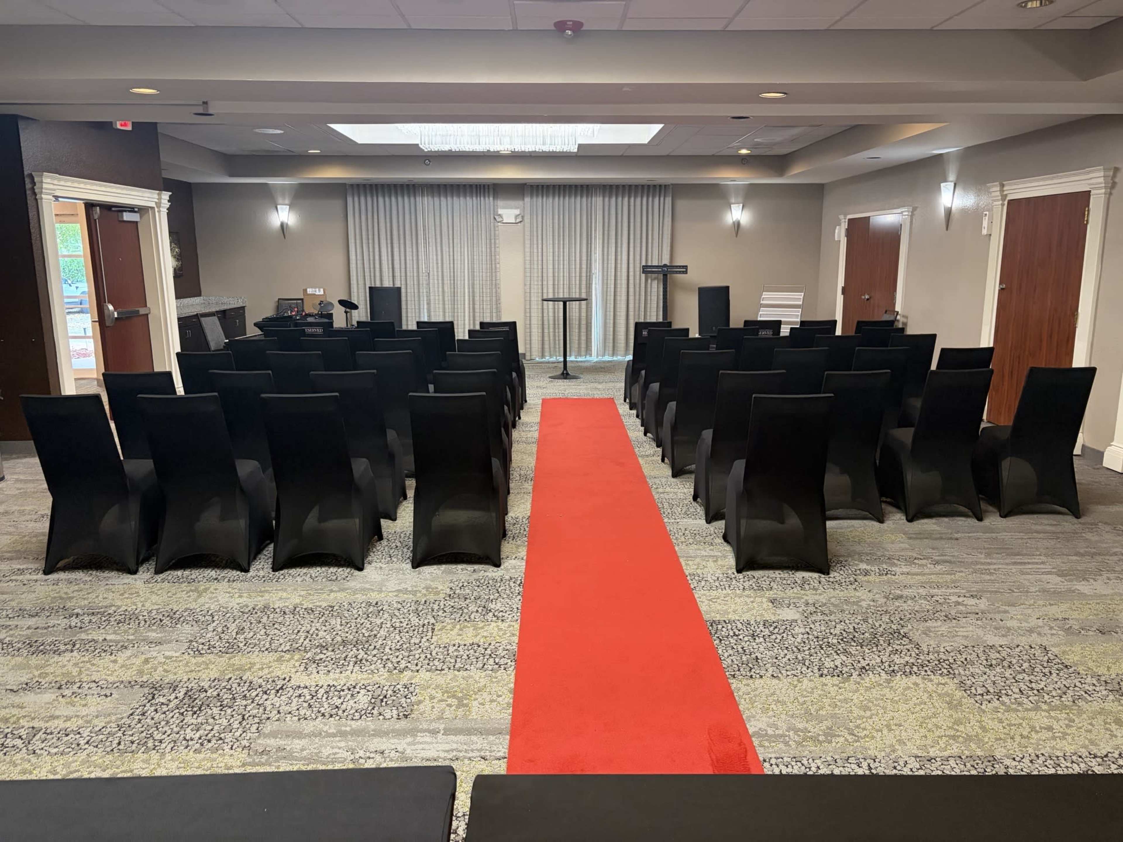 The image shows a conference room set up with rows of black chairs facing a small stage, with a red carpet in the center.