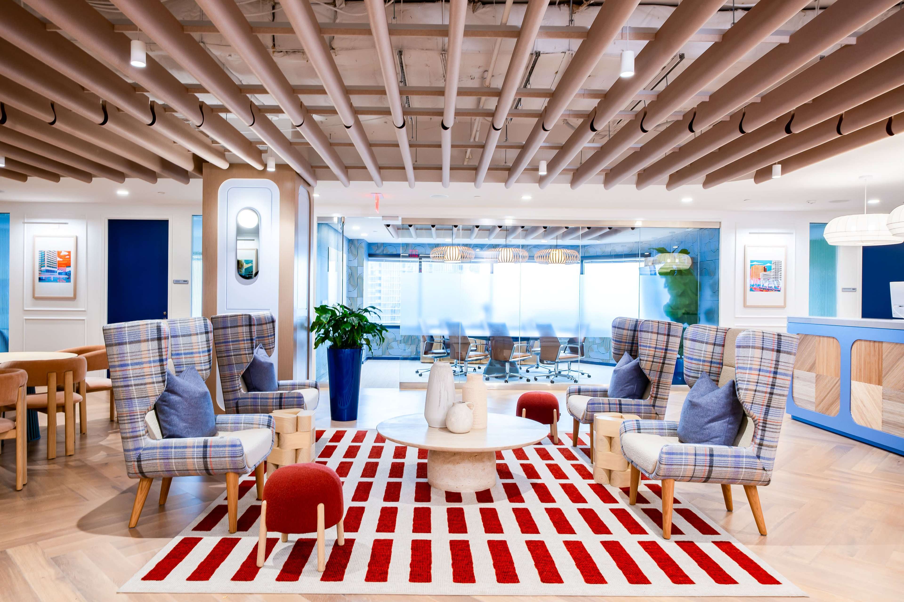 The image shows a modern office lobby with two checkered armchairs, a circular coffee table, and a red and white striped rug, alongside a conference area in the background.