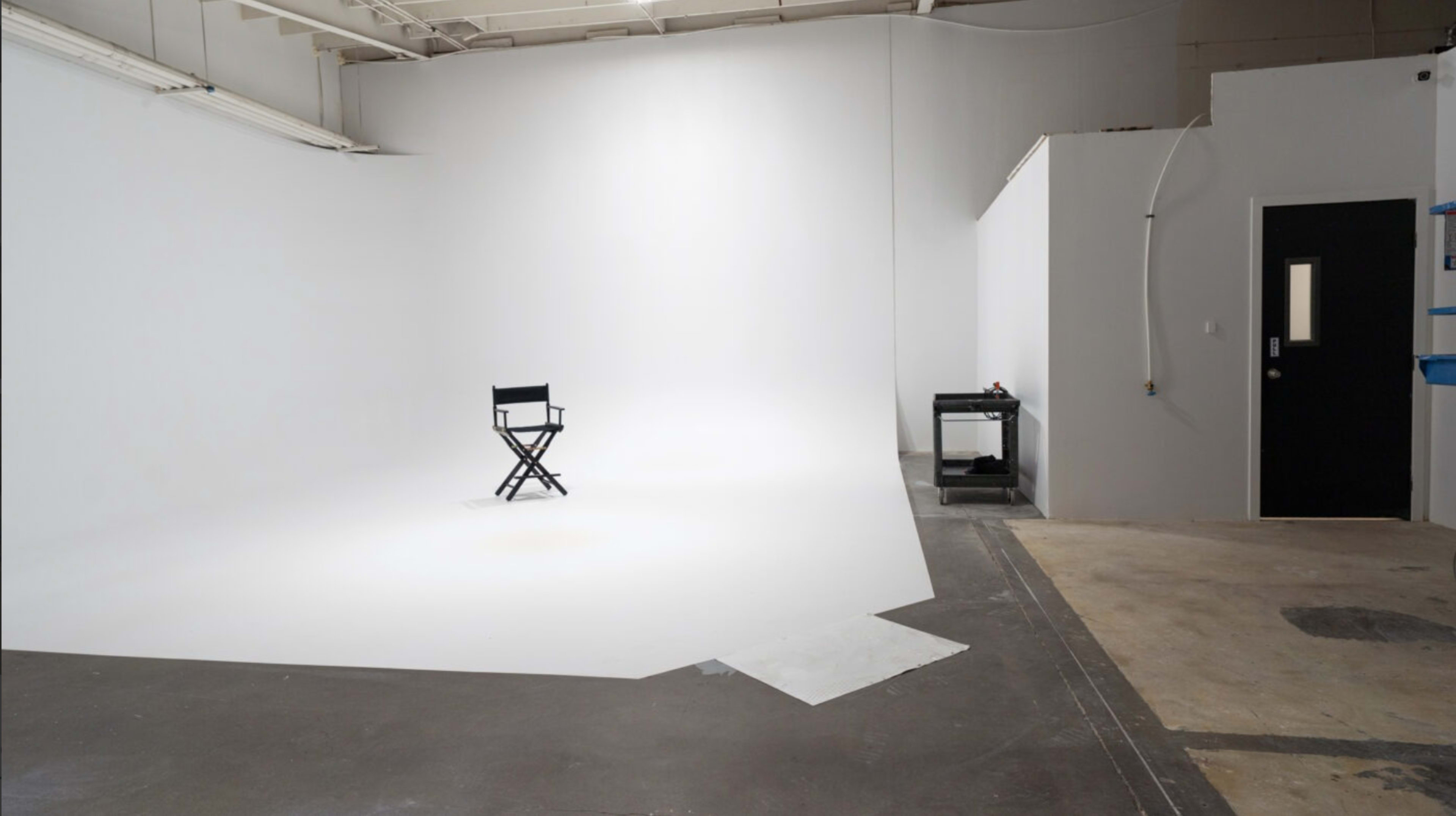 A single director's chair is positioned on a vast, empty white backdrop within a studio space.
