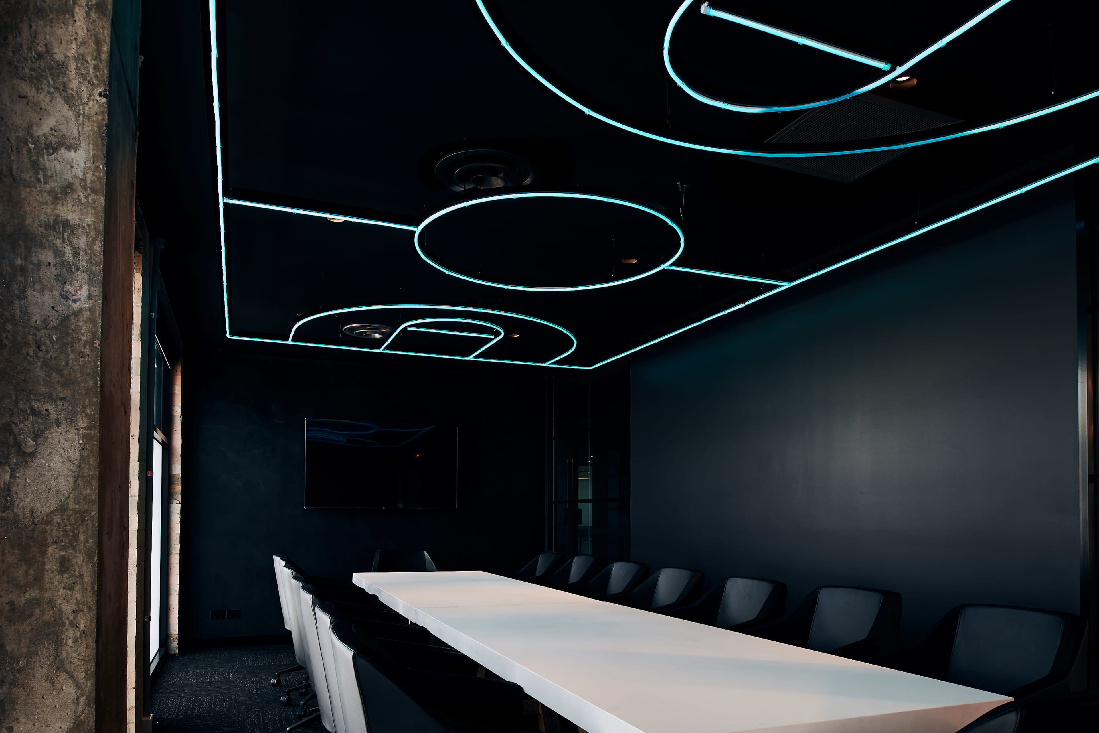 A large conference room features a long white table surrounded by black chairs, with a ceiling illuminated by glowing blue lines in circular and abstract patterns.