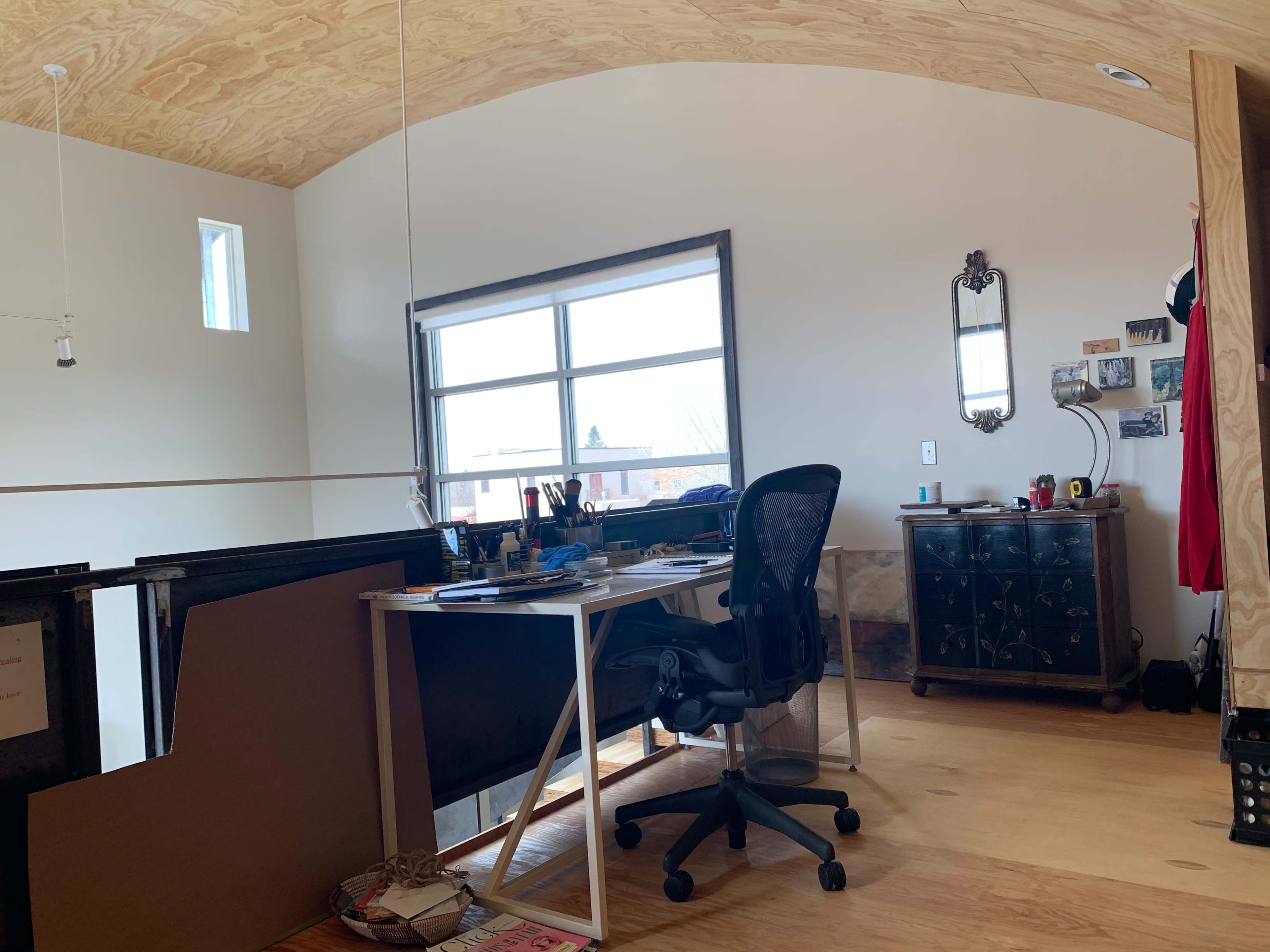 A home office with a desk, a rolling chair, and a large window letting in natural light.