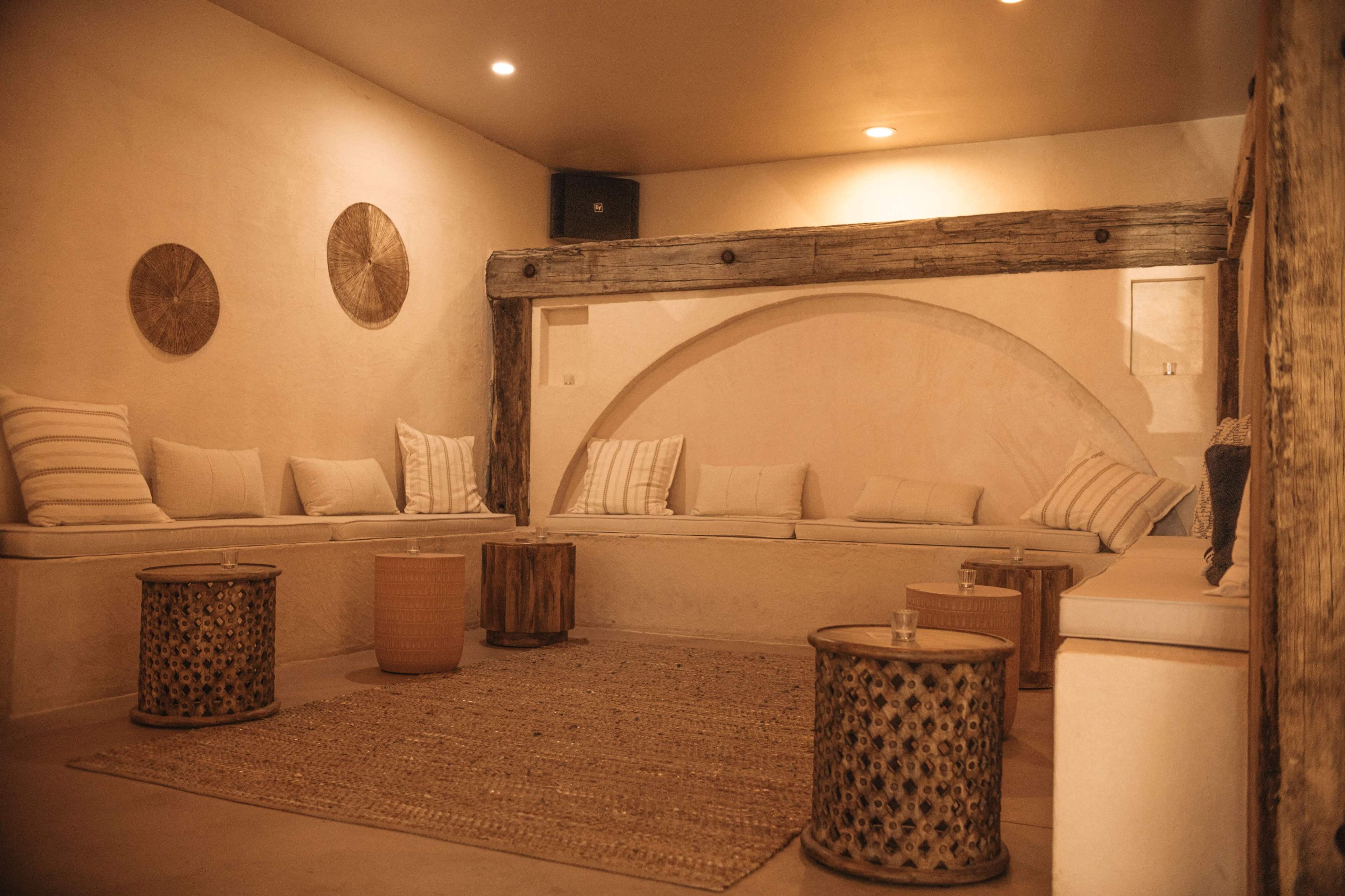 A minimalist lounge area with a curved alcove, wooden beams, low seating, and decorative woven wall art.