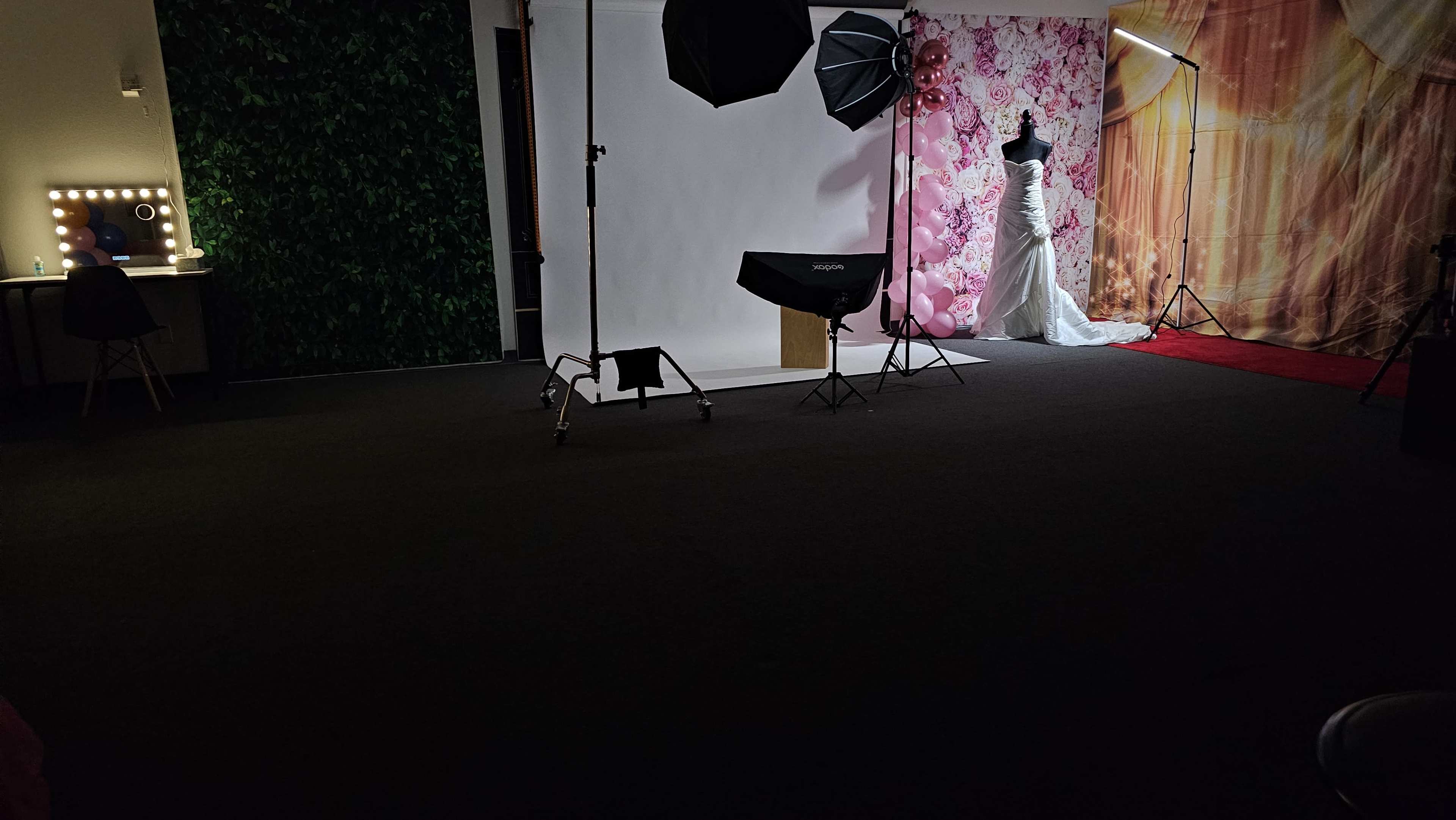 The image shows a photography studio setup with a mannequin dressed in a white gown, surrounded by lighting equipment and pastel floral backdrops.