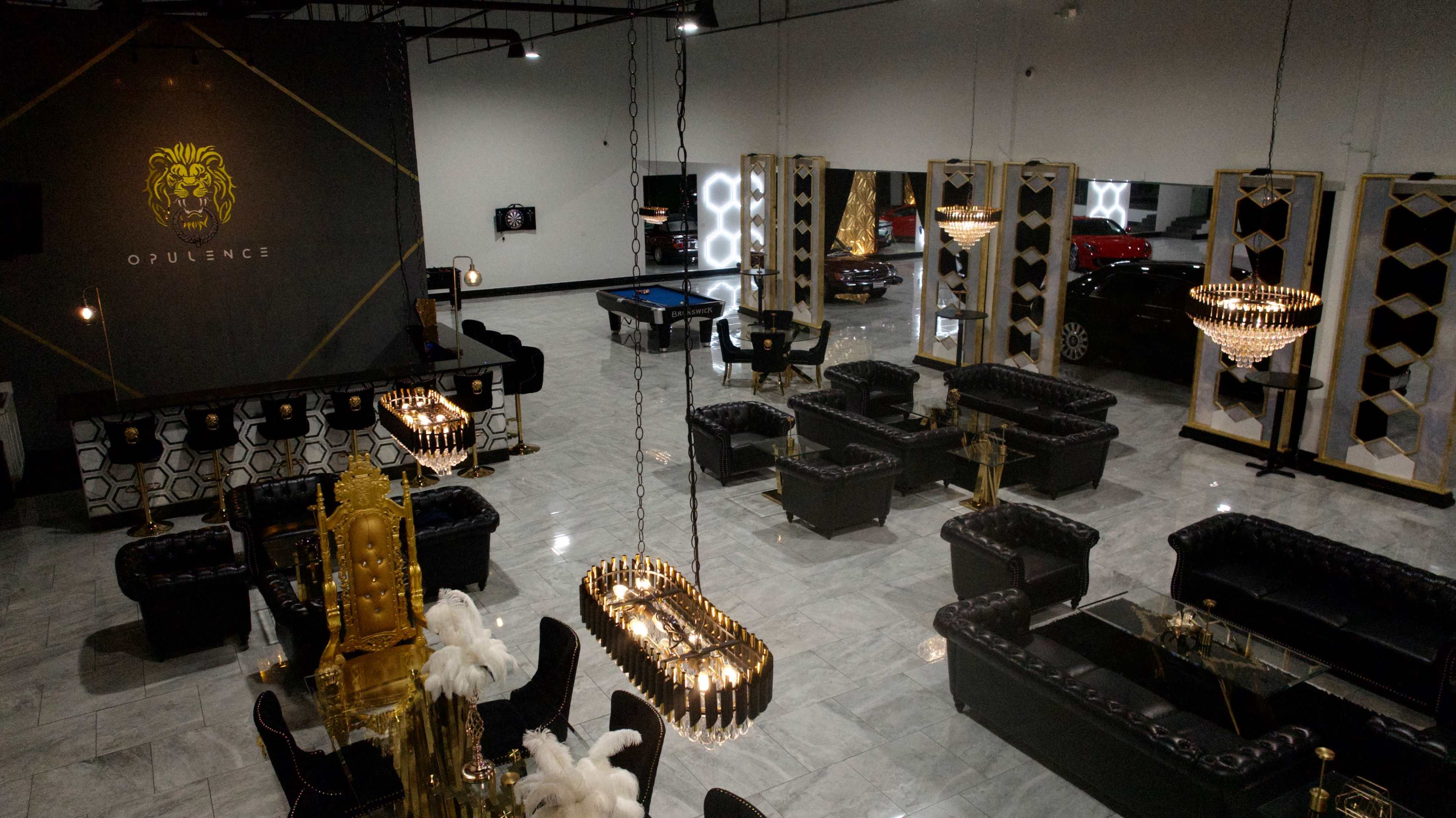 The image depicts a spacious, elegantly designed lounge area with black leather furniture, ornate chandeliers, and a gold and black color scheme.