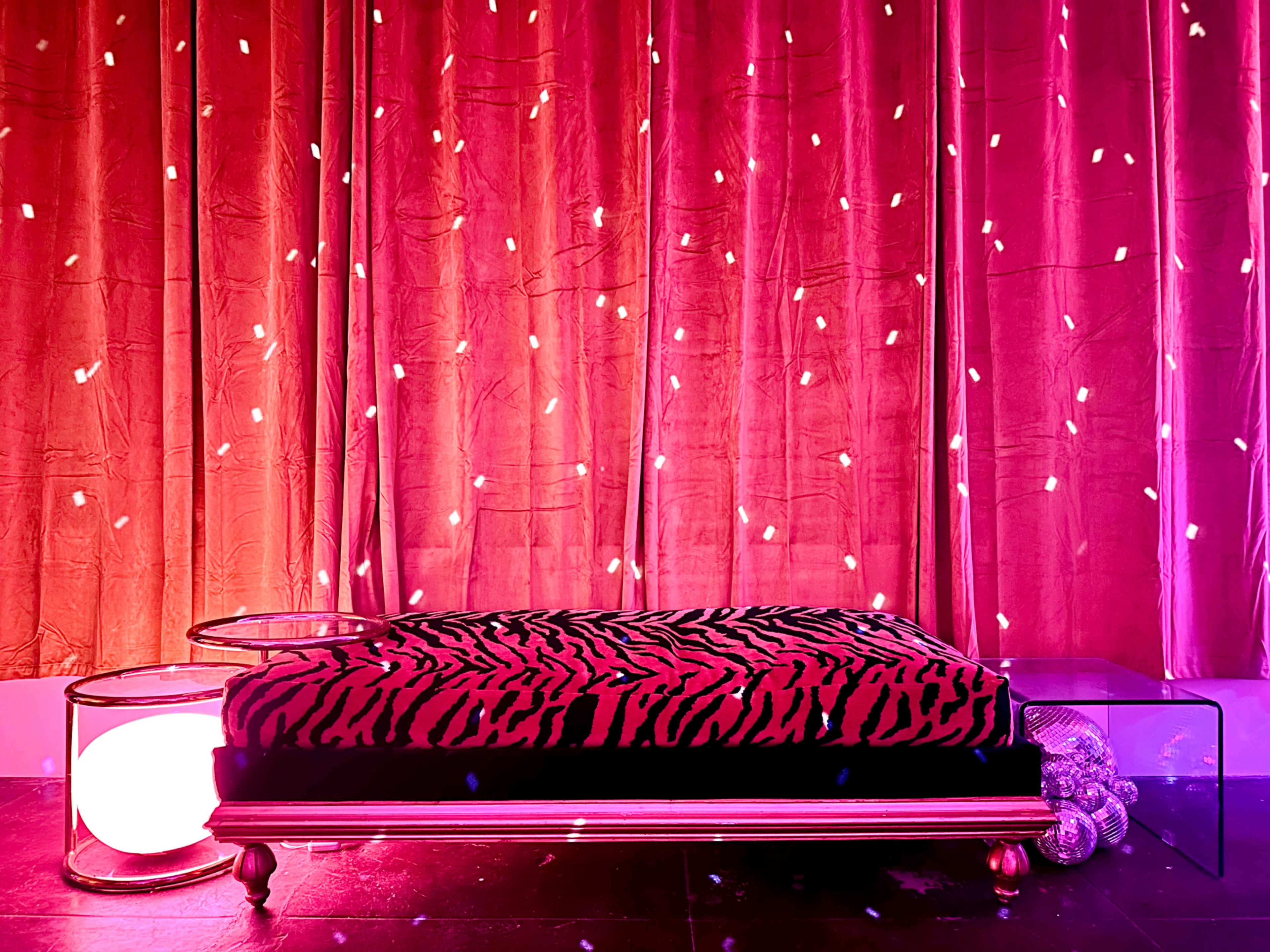 A zebra-striped cushion on a metallic frame, placed in front of a backdrop of red curtains adorned with fairy lights.