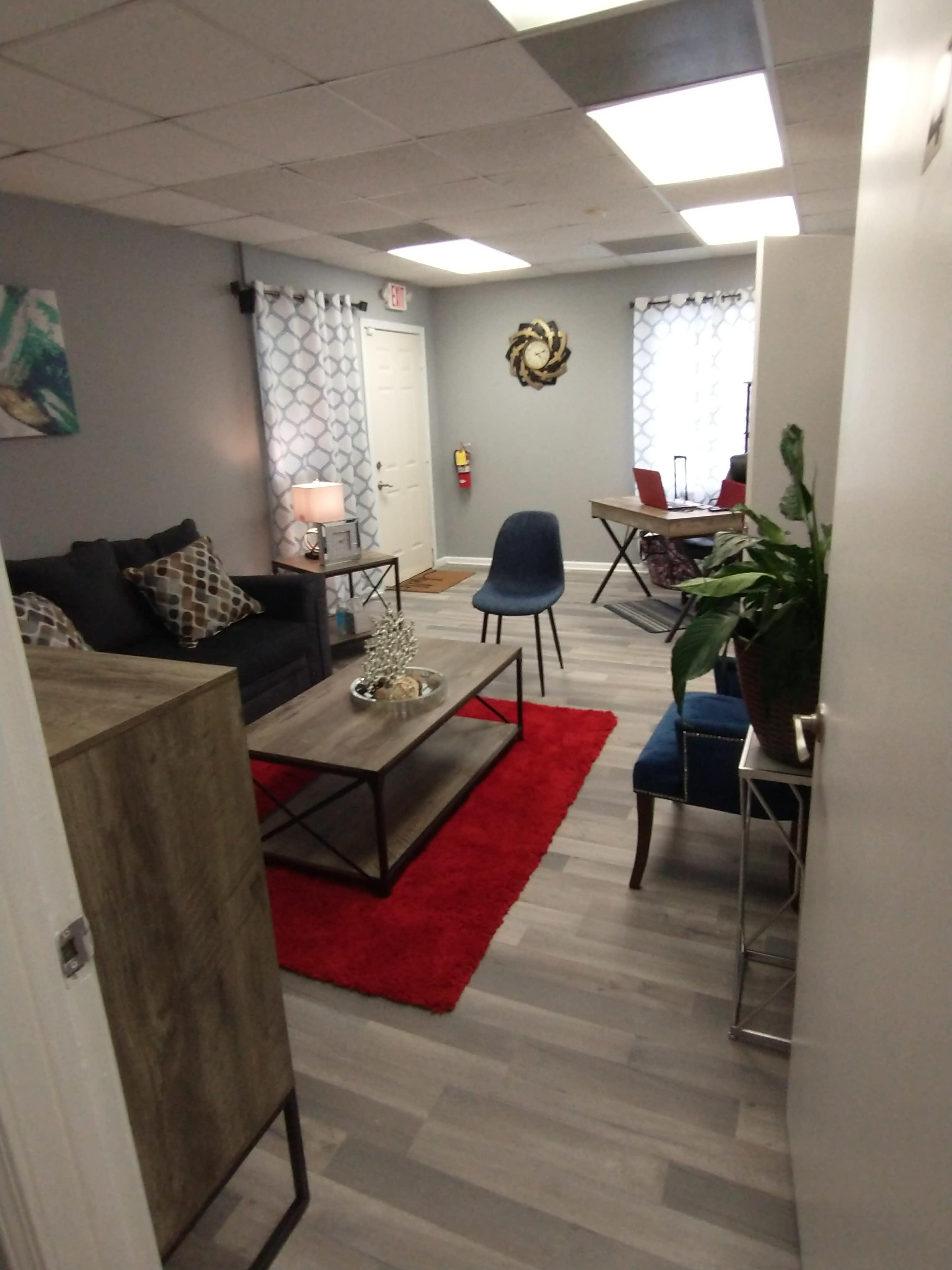 A modern, welcoming office space with a seating area featuring a sofa, coffee table, and decorative rug, alongside a small dining table and chairs.