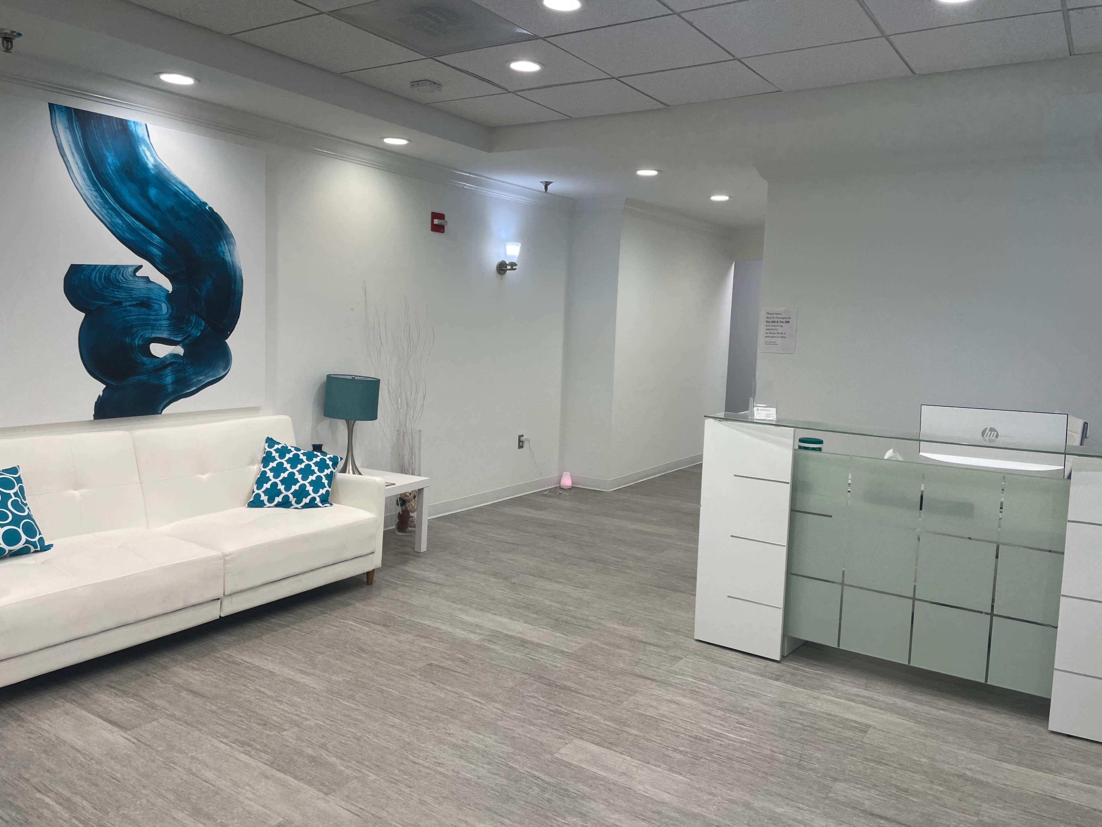 A modern reception area with a white sofa adorned with blue cushions, a minimalist front desk, and light wooden flooring.