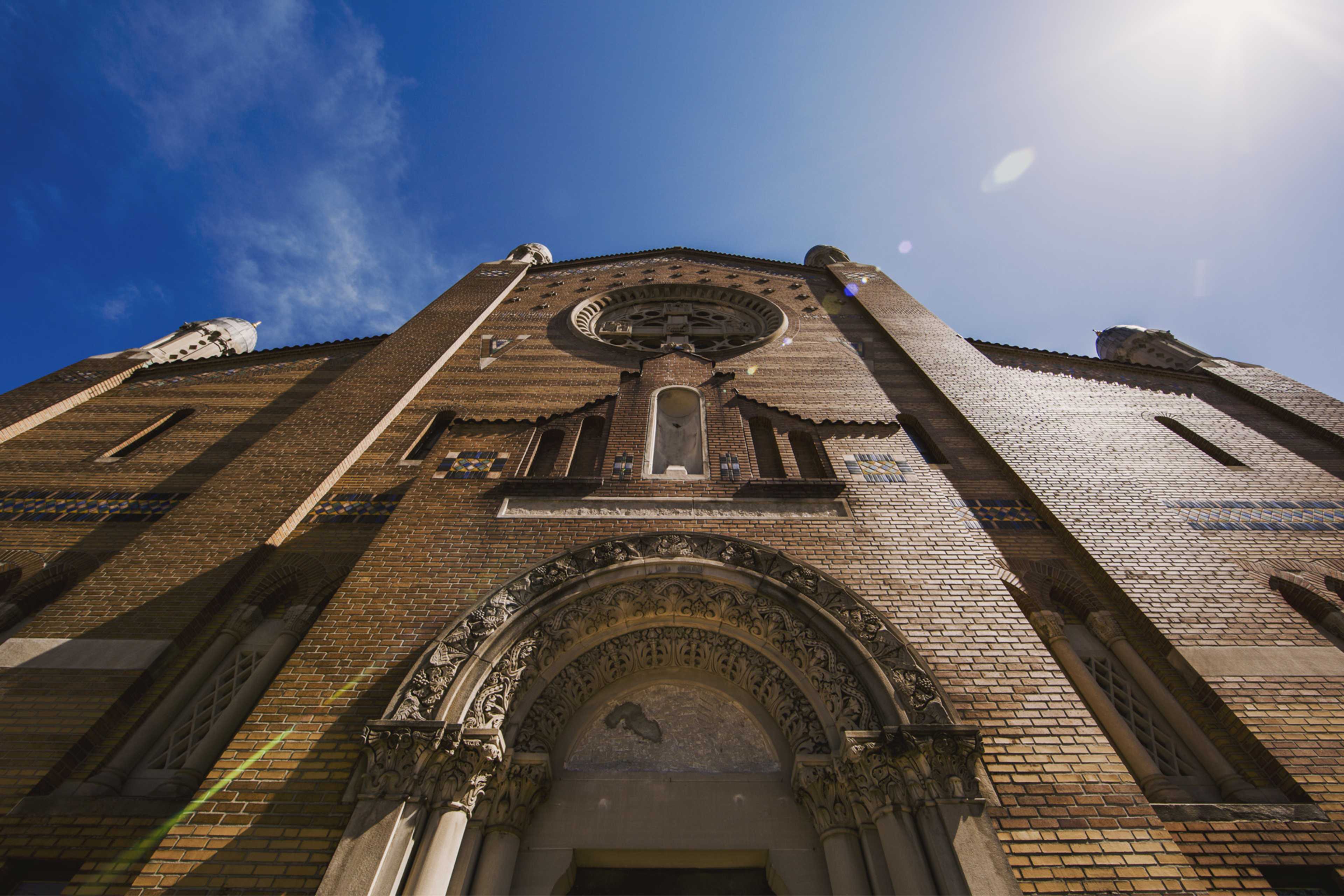 The intricate facade of a brick church, captured from a low angle against a clear blue sky.