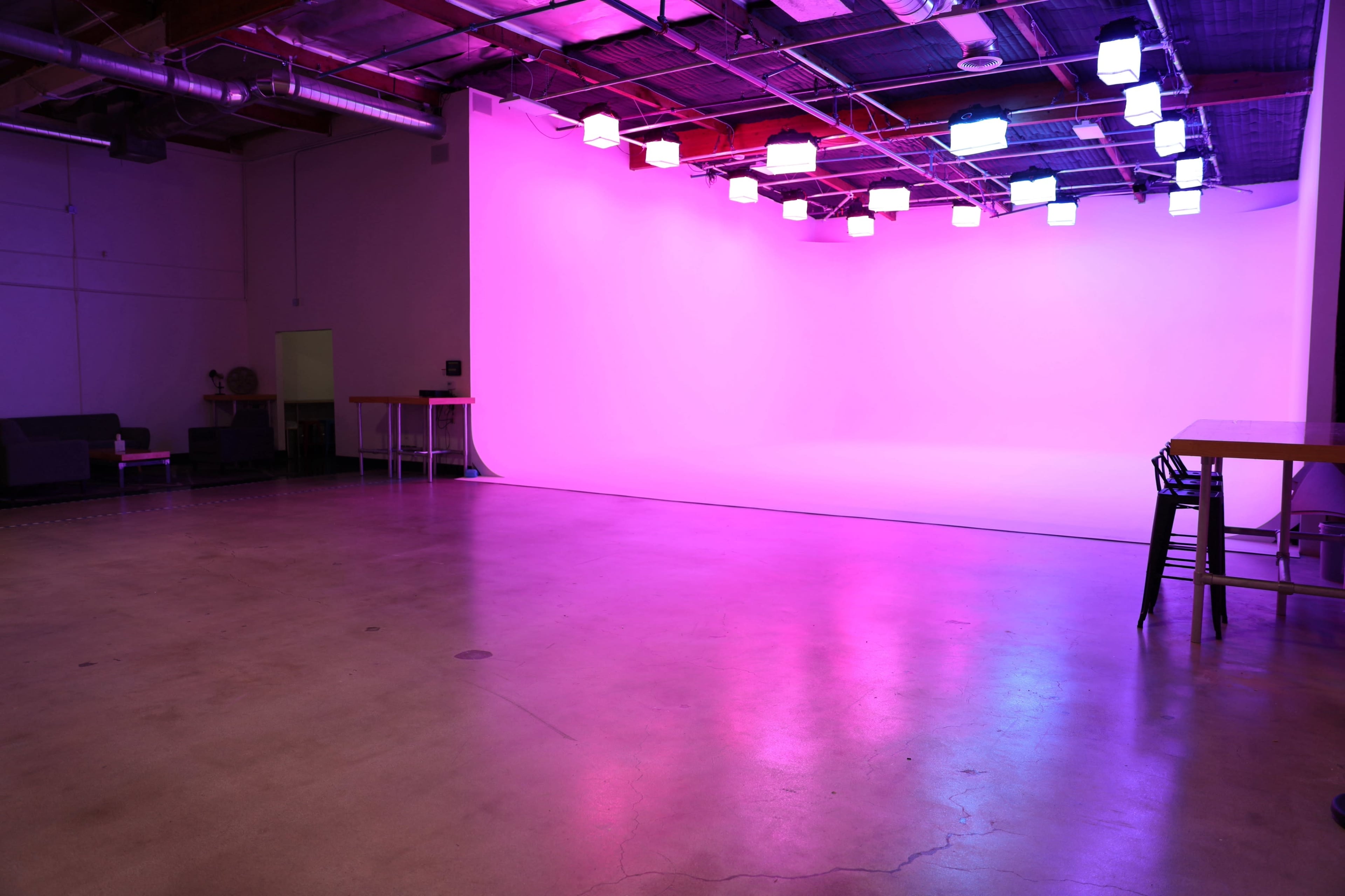 An empty studio space with a smooth floor and a brightly lit backdrop featuring purple hues.