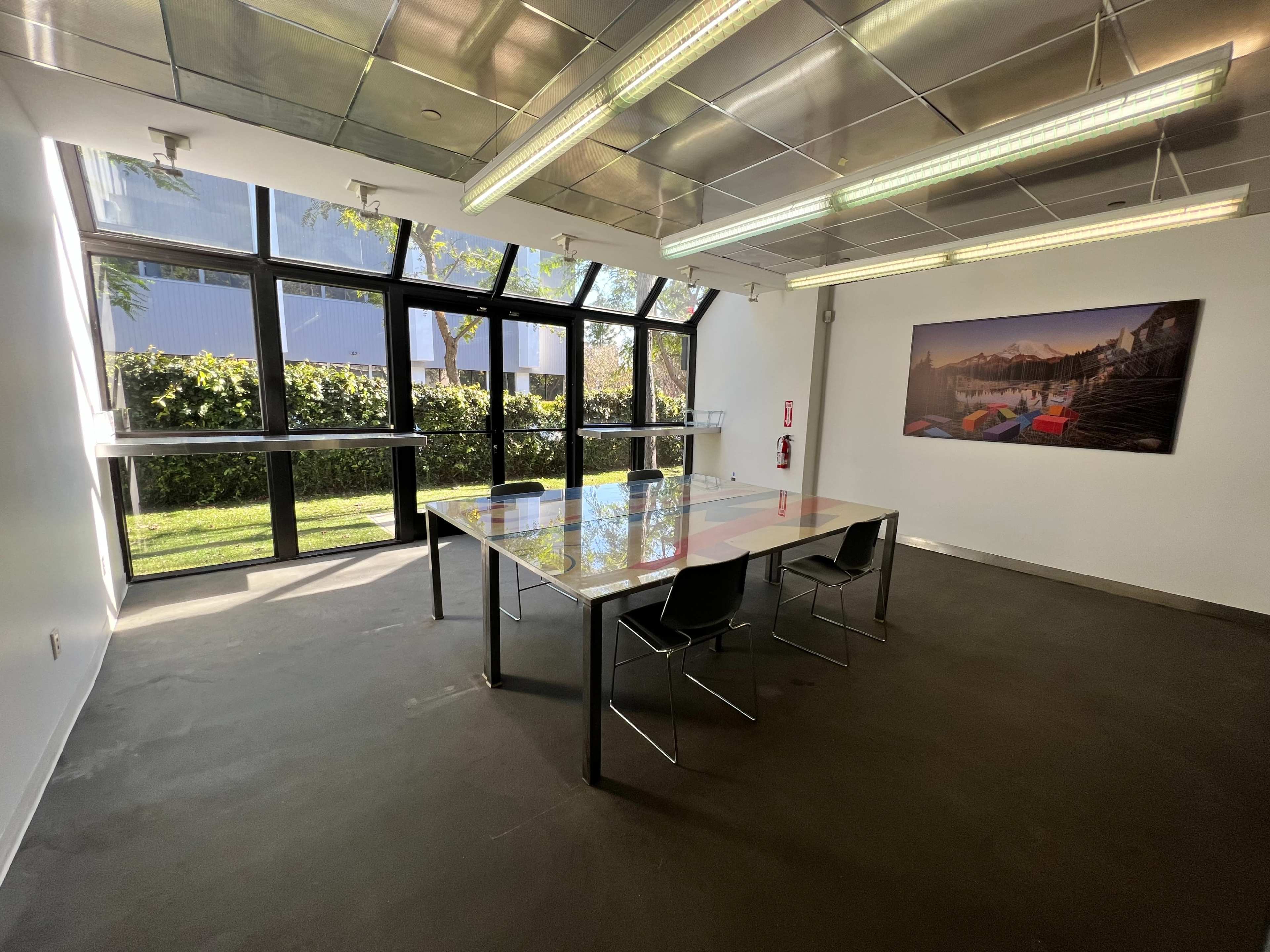 A bright meeting room features a large table, several chairs, and large windows overlooking a green area.