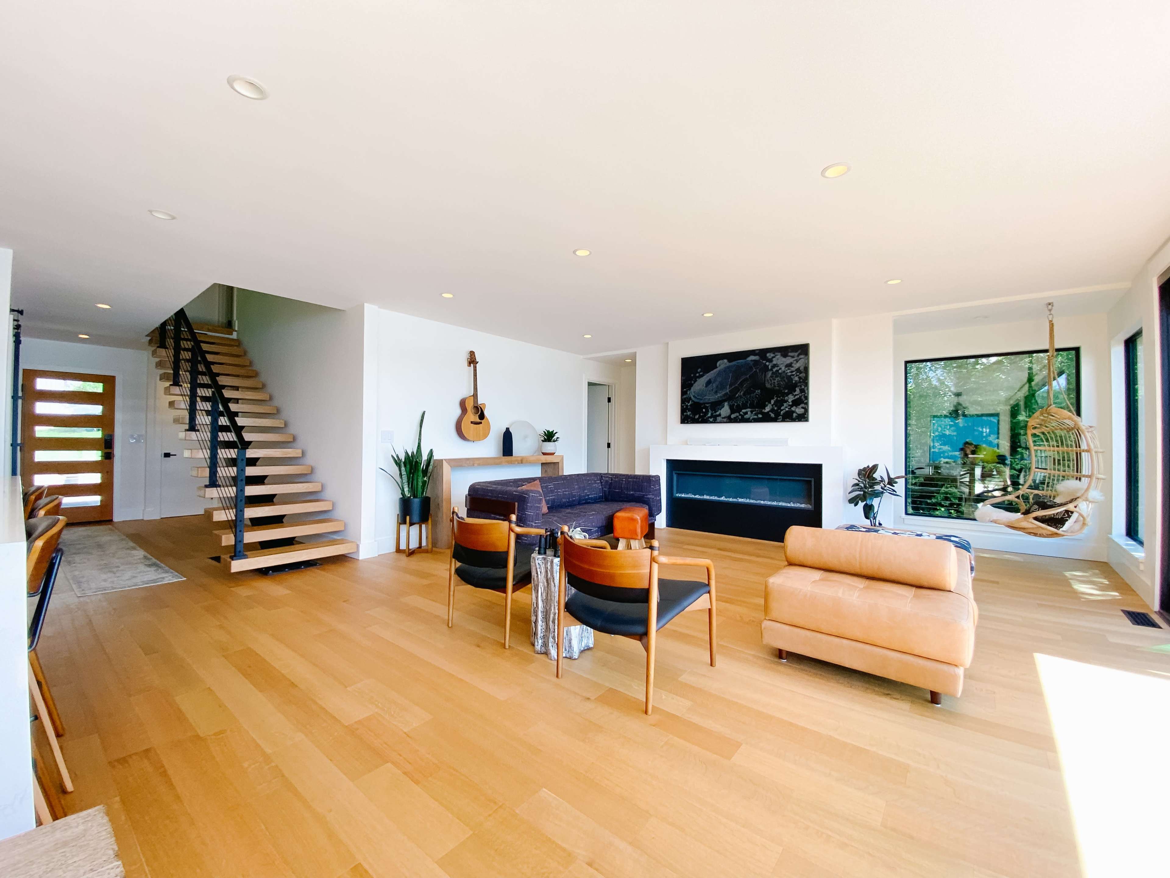 A modern living room with hardwood floors, a fireplace, a guitar on the wall, and a staircase leading to an upper level.