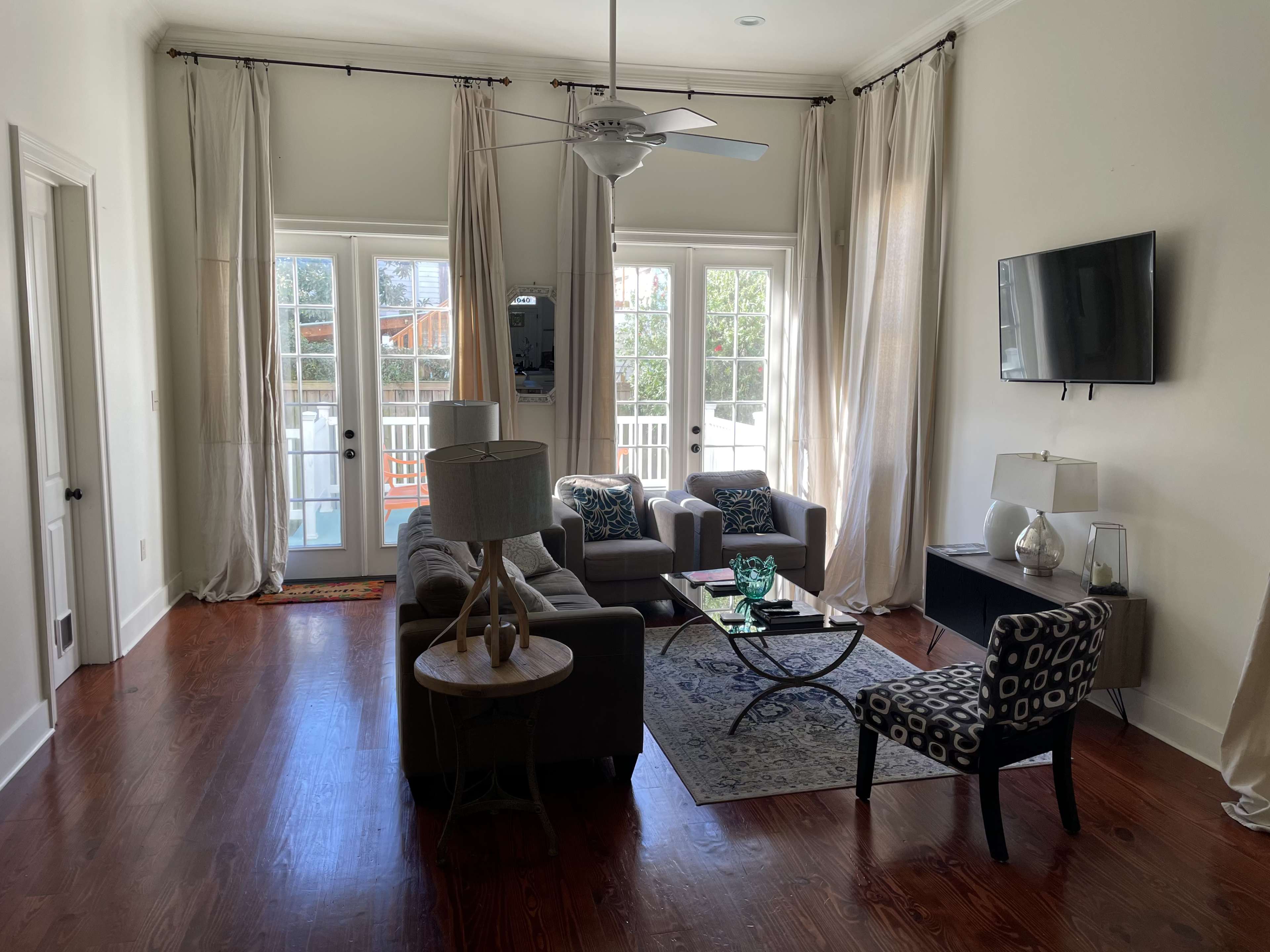 The living room features a seating arrangement with a sofa, two chairs, a coffee table, and large windows that open to a porch.