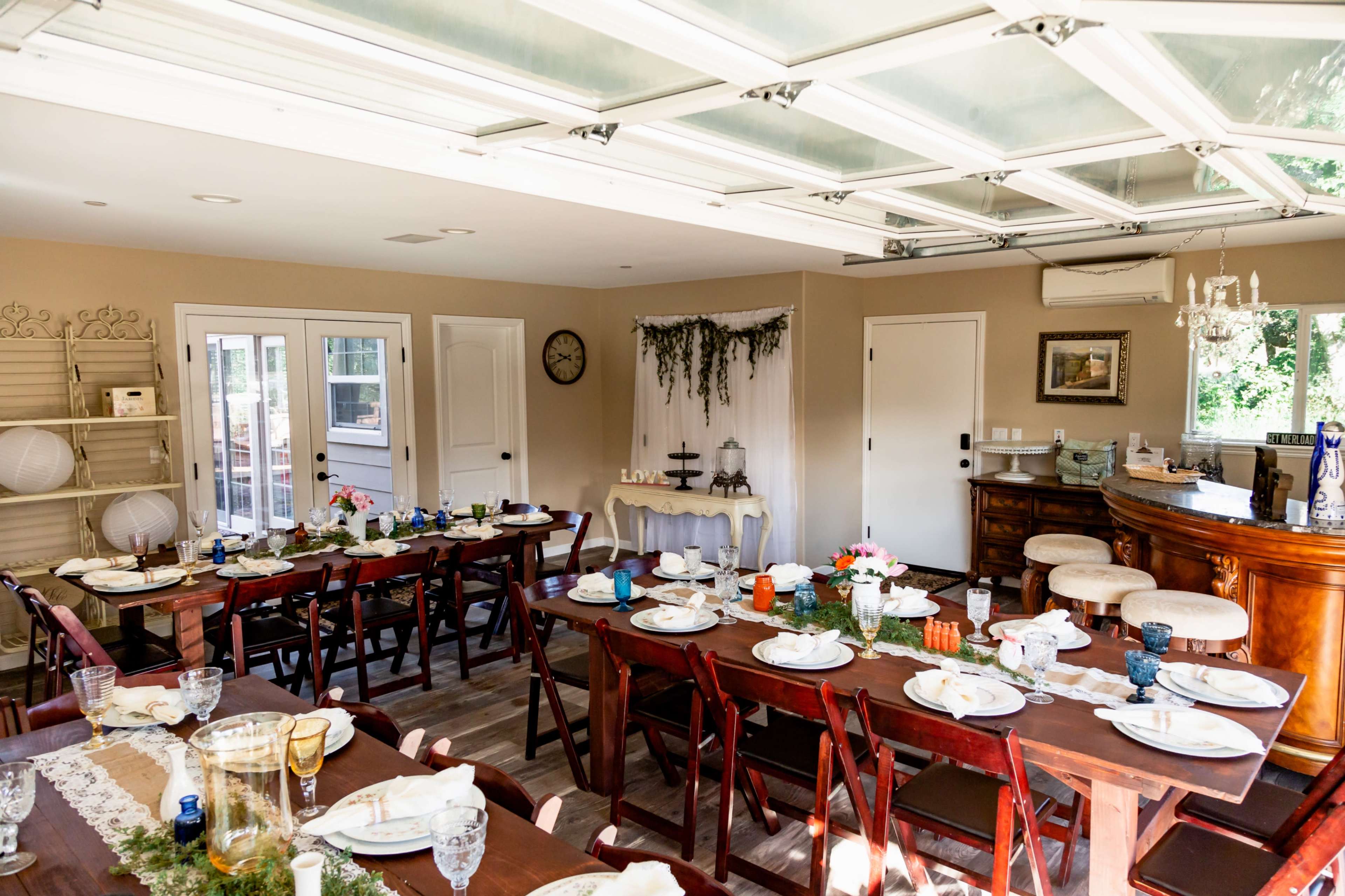 A dining room is set up with multiple tables arranged for a meal, decorated with place settings and floral arrangements.