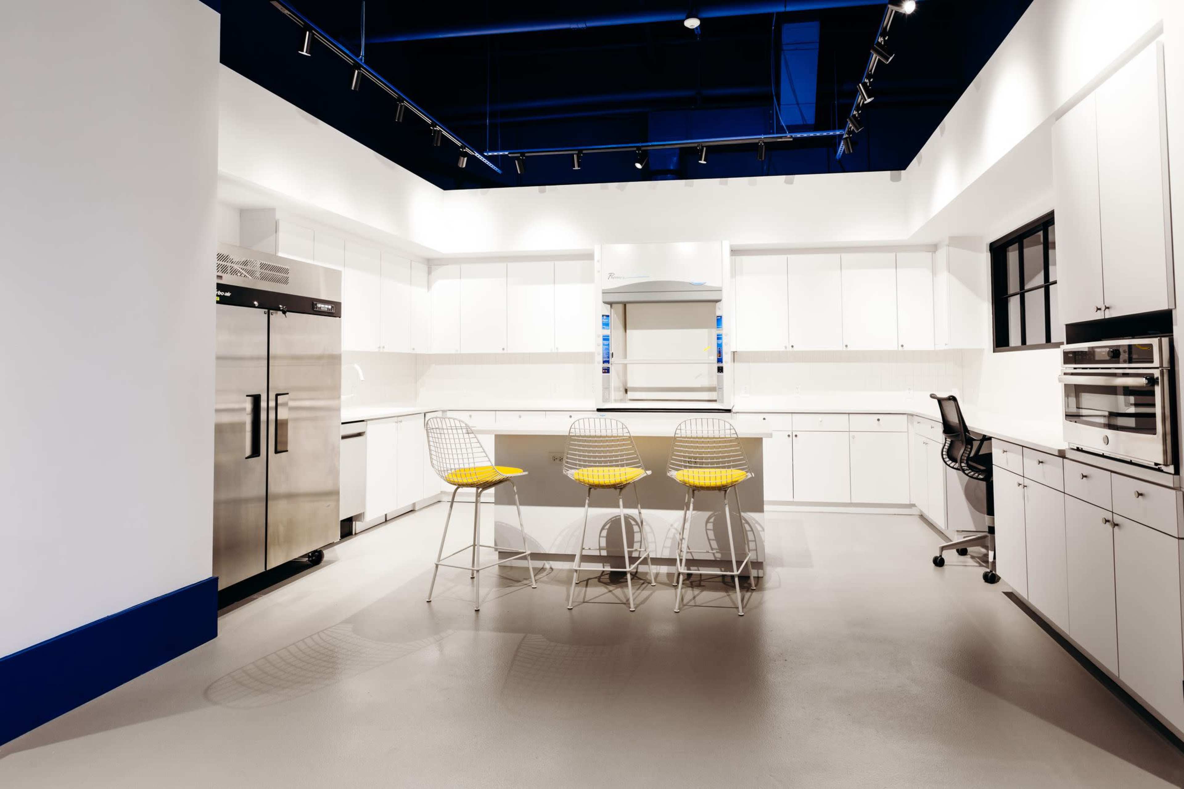 A modern kitchen features white cabinetry, stainless steel appliances, and a central island with four wire bar stools.