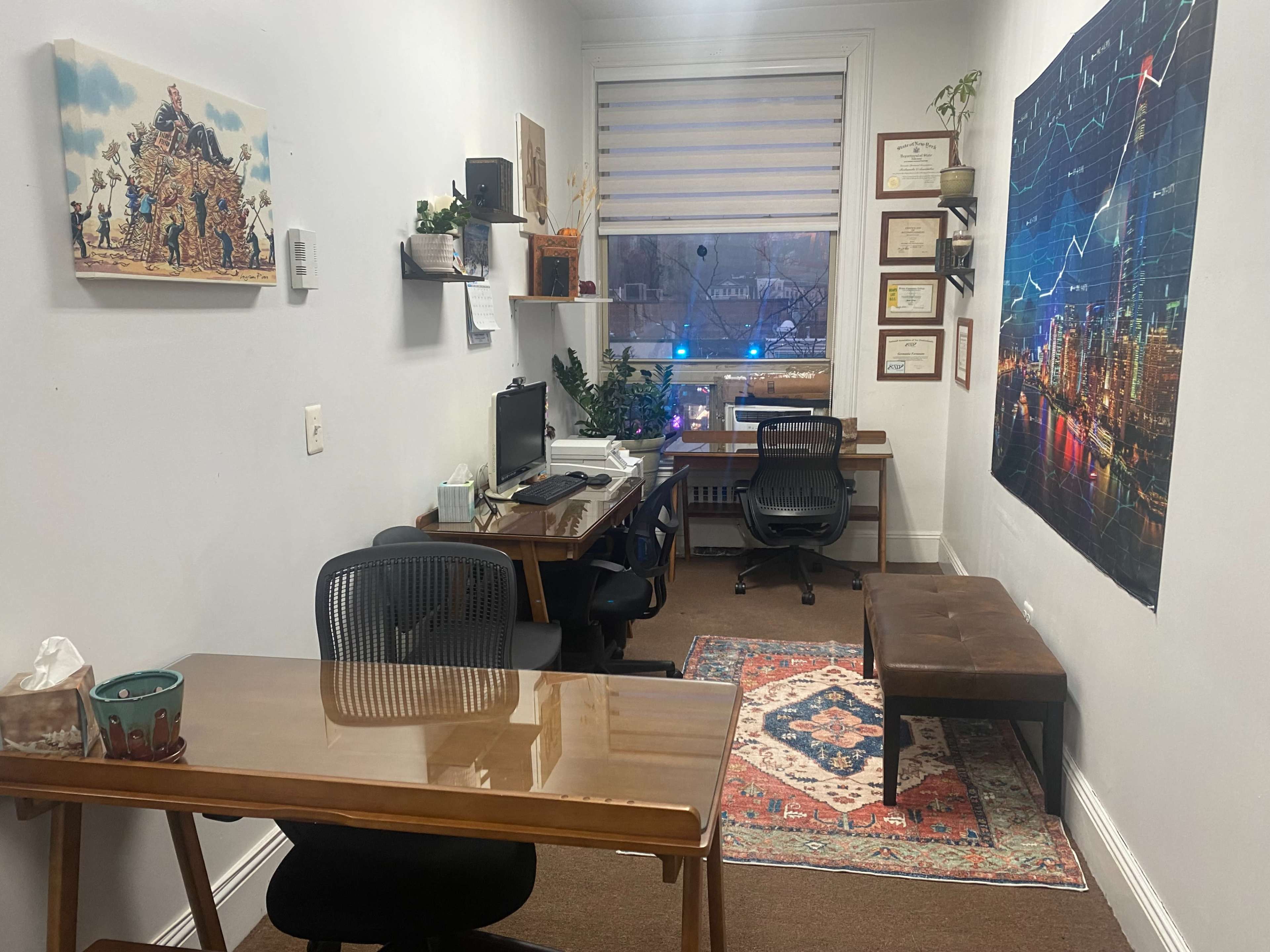 A small office space featuring a desk with a computer, a bench, a wall adorned with framed certificates, and a large graphic of a city skyline with financial charts.