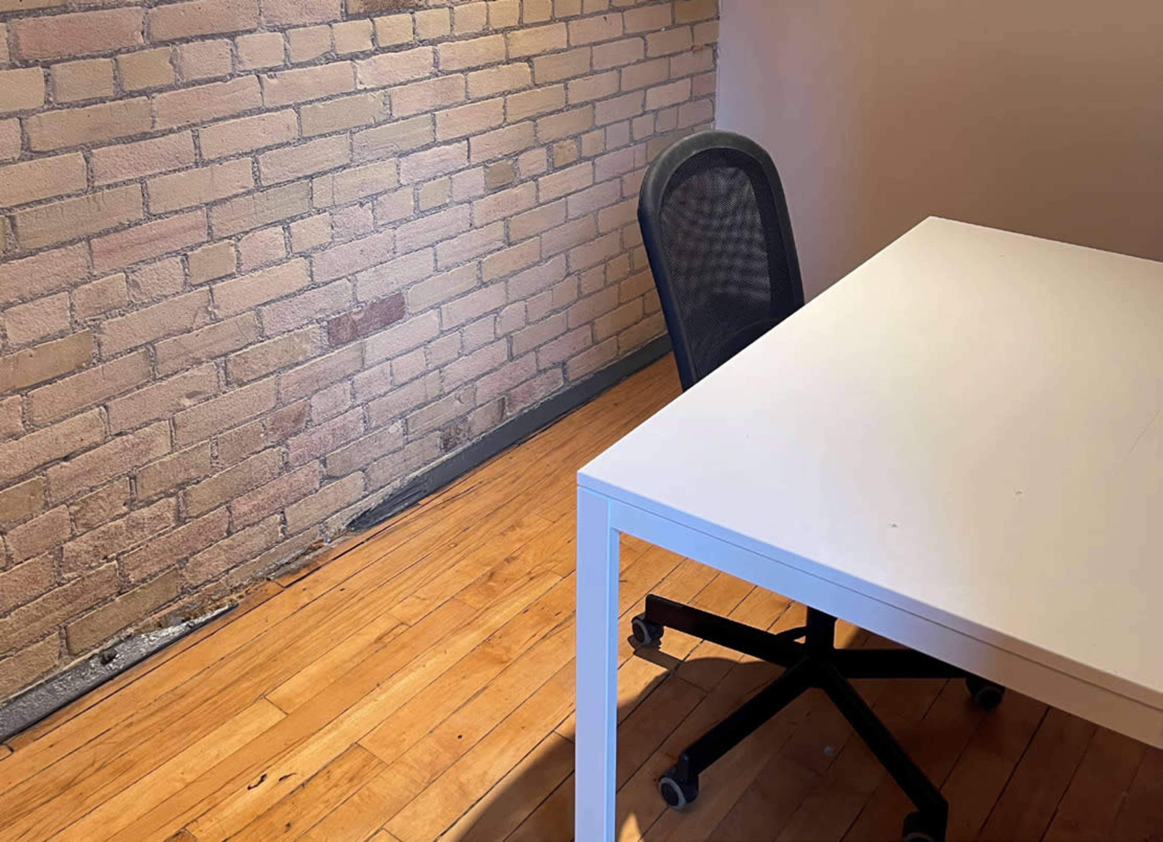 A simple desk and a chair in a room with a brick wall and hardwood floor.