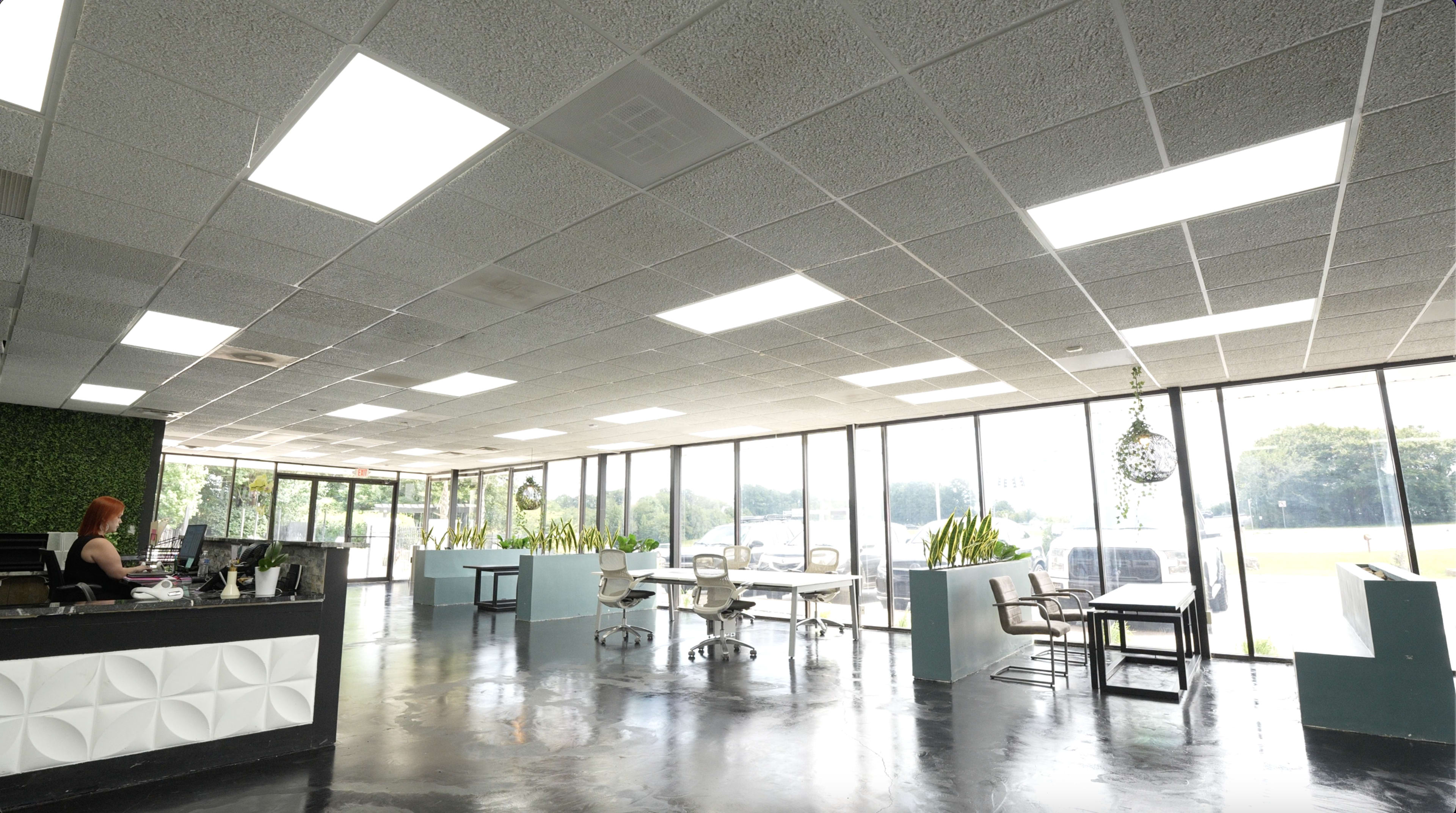 A modern office space features a reception area with a desk, several workstations, and large windows letting in natural light.