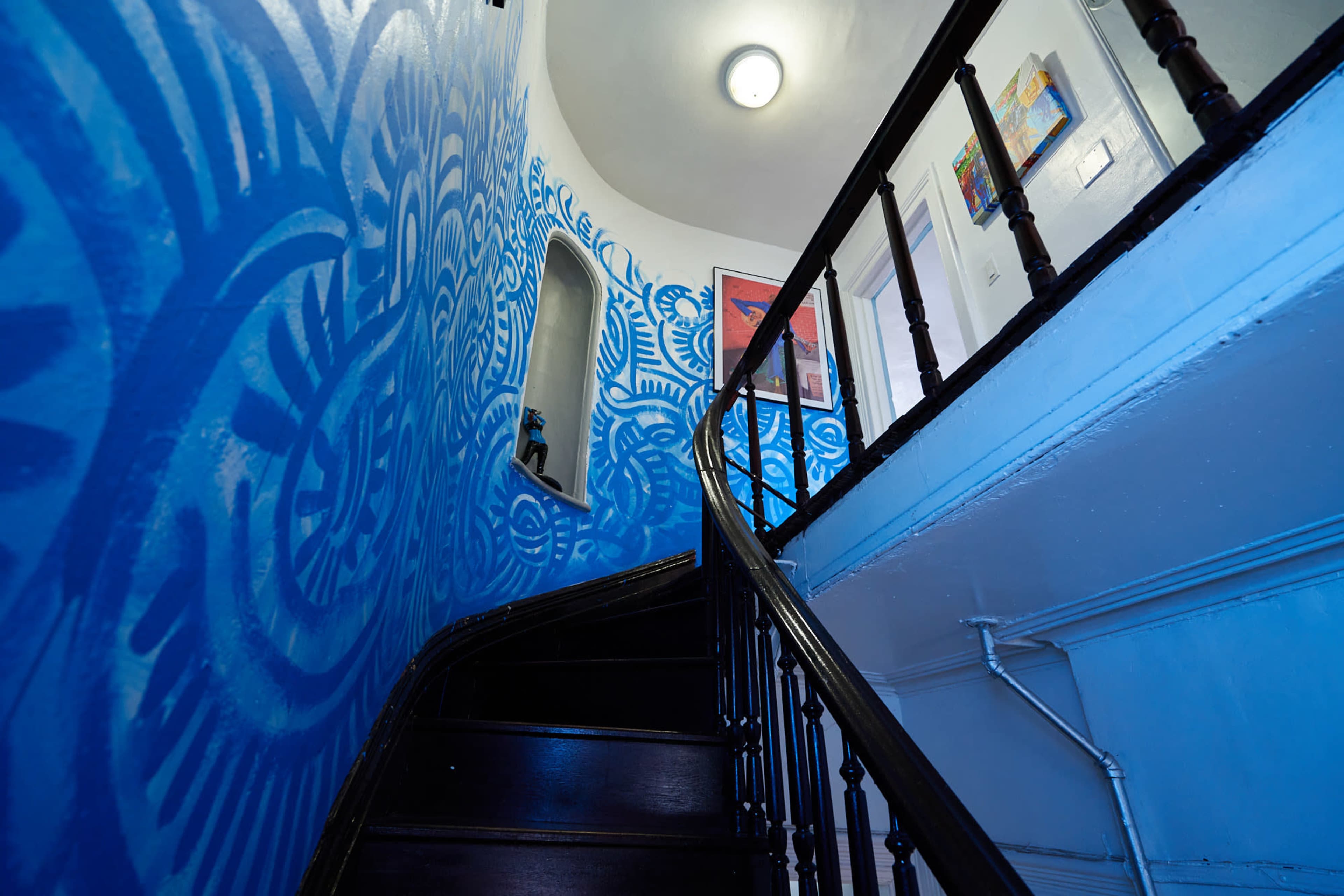A spiral staircase ascends alongside a vibrant blue mural on the wall.