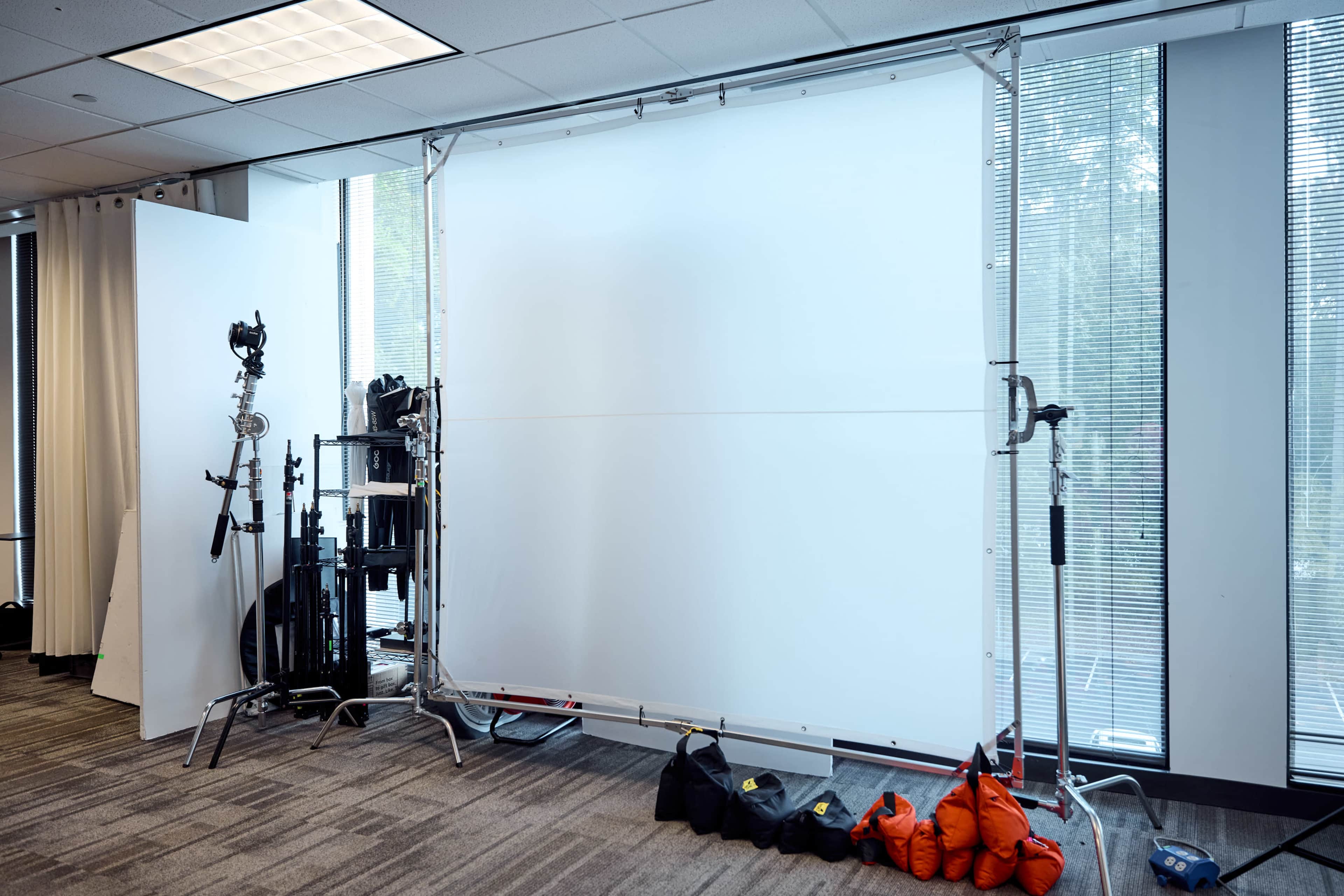 A photography setup is displayed in an indoor space, featuring a large white backdrop supported by a metal frame and various lighting equipment.