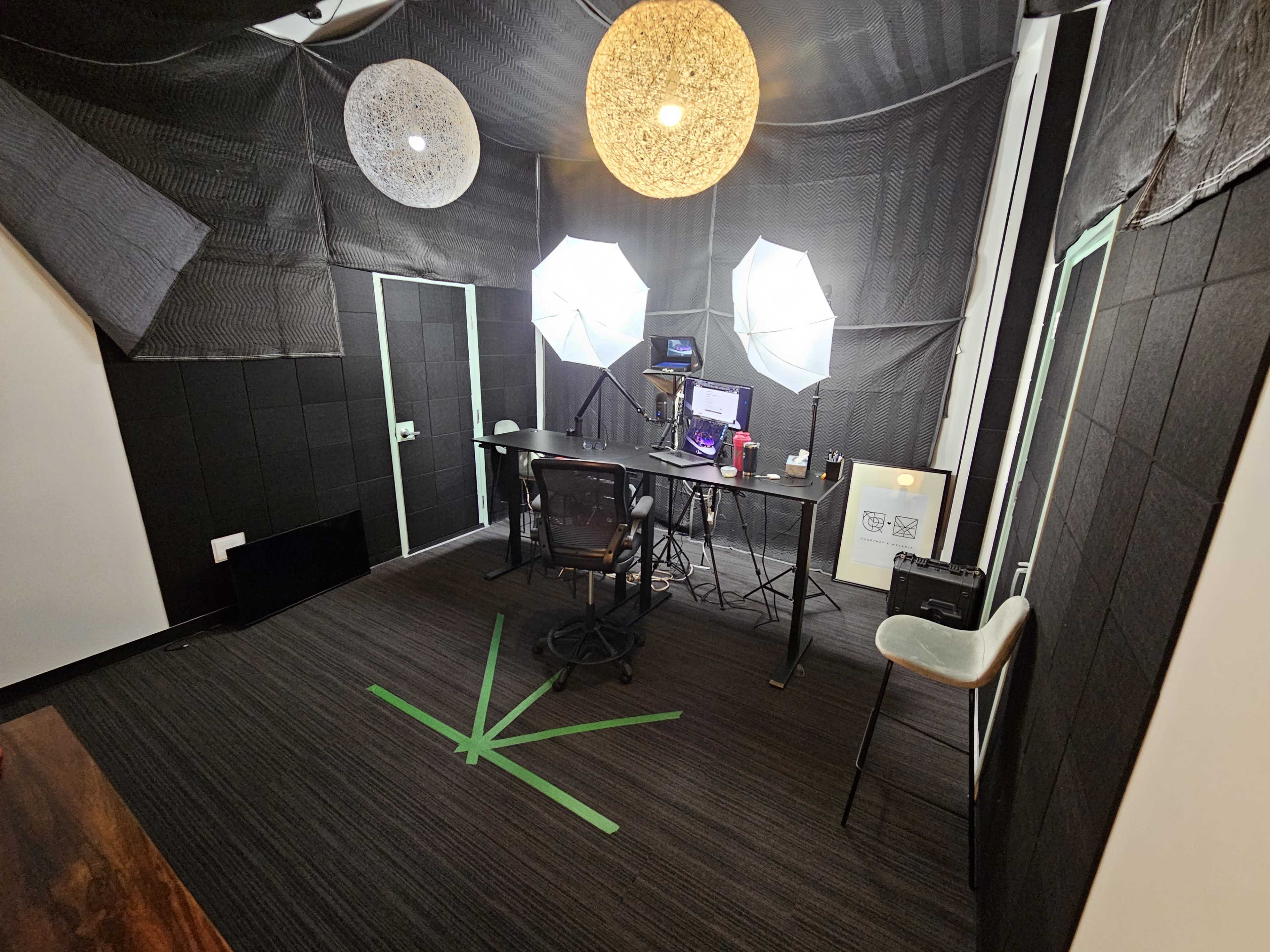 A small studio space features a desk with a computer and equipment, flanked by large softbox lights and decorated with hanging circular lamps.