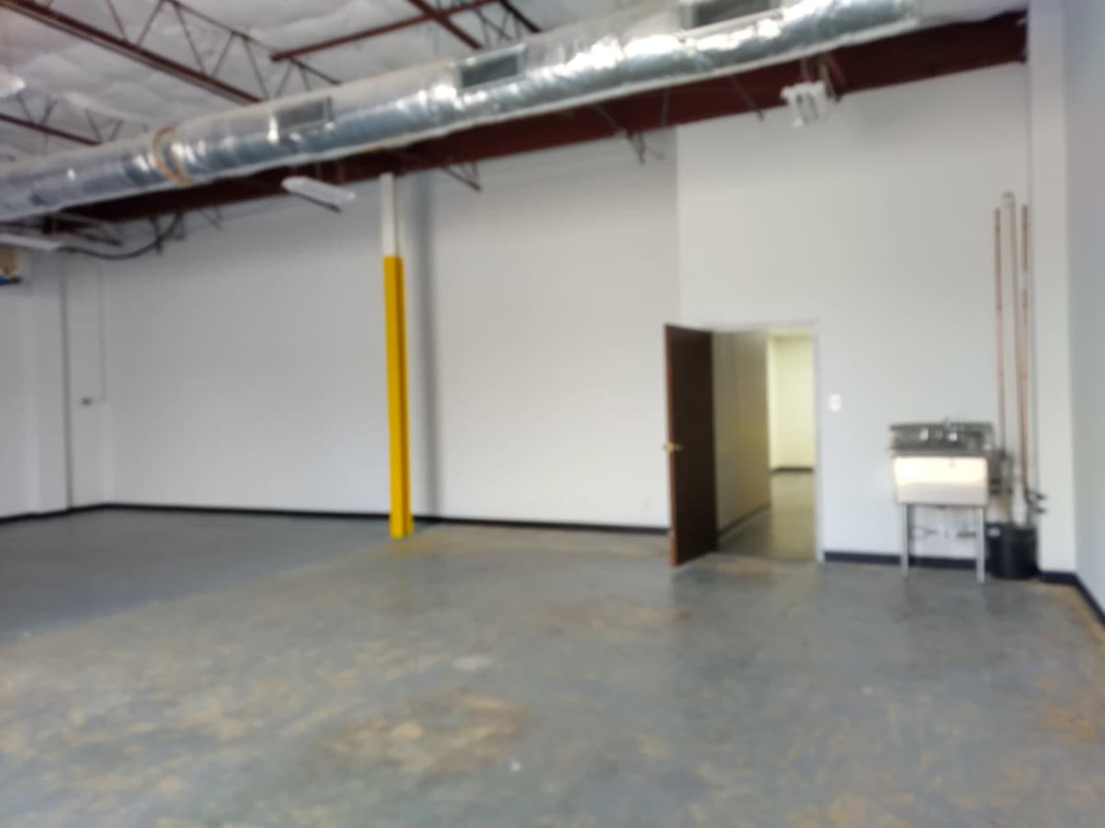 The image shows a large, empty industrial space with a gray floor, white walls, and a doorway leading to another room.