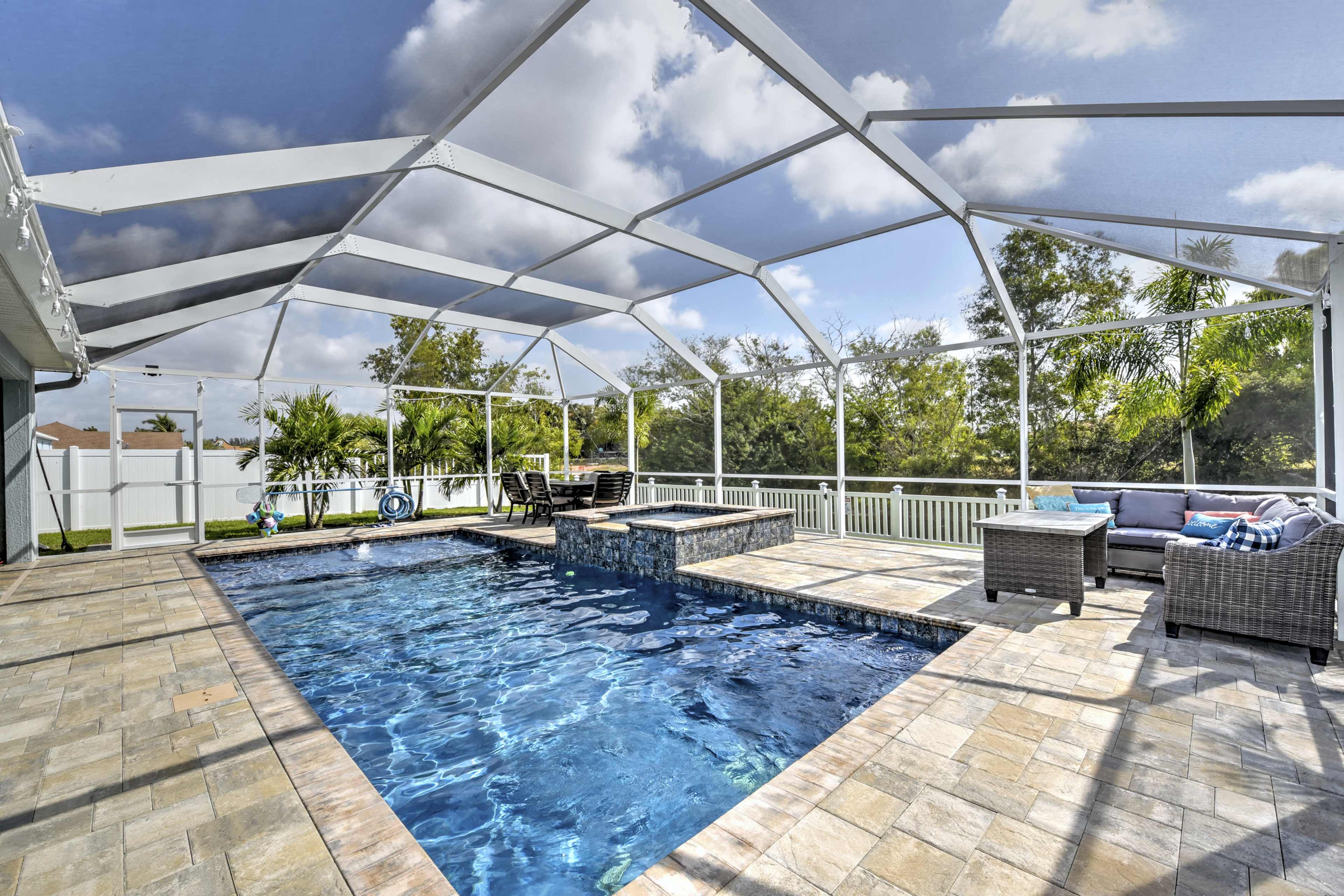 The image shows a large, open pool area with a screened enclosure, featuring a rectangular swimming pool and a patio furnished with seating.