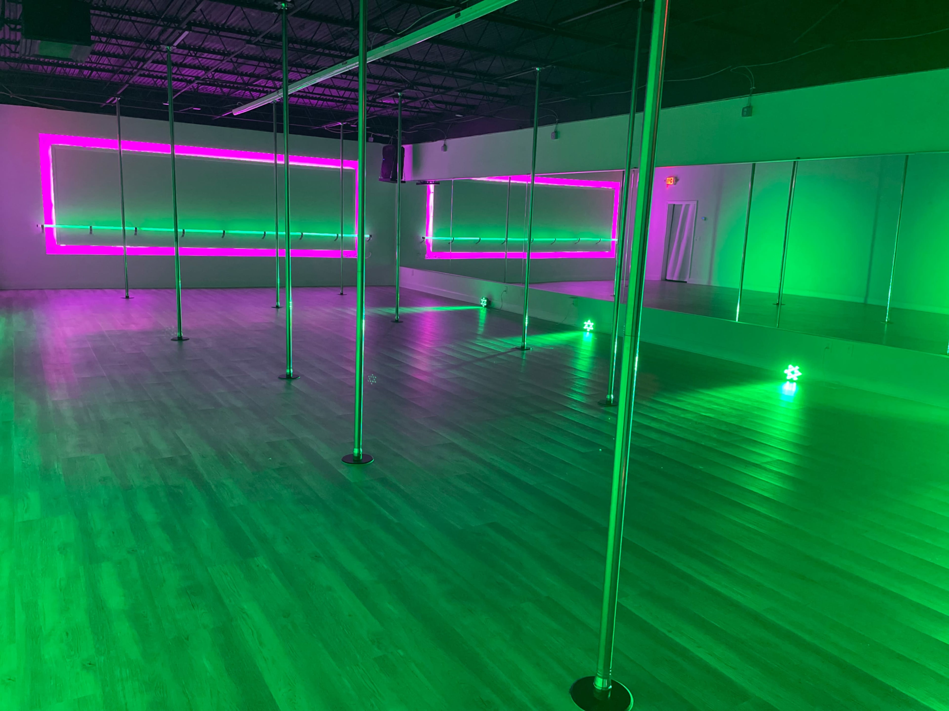 The image shows a spacious dance studio with several vertical poles and green neon lighting along the walls.