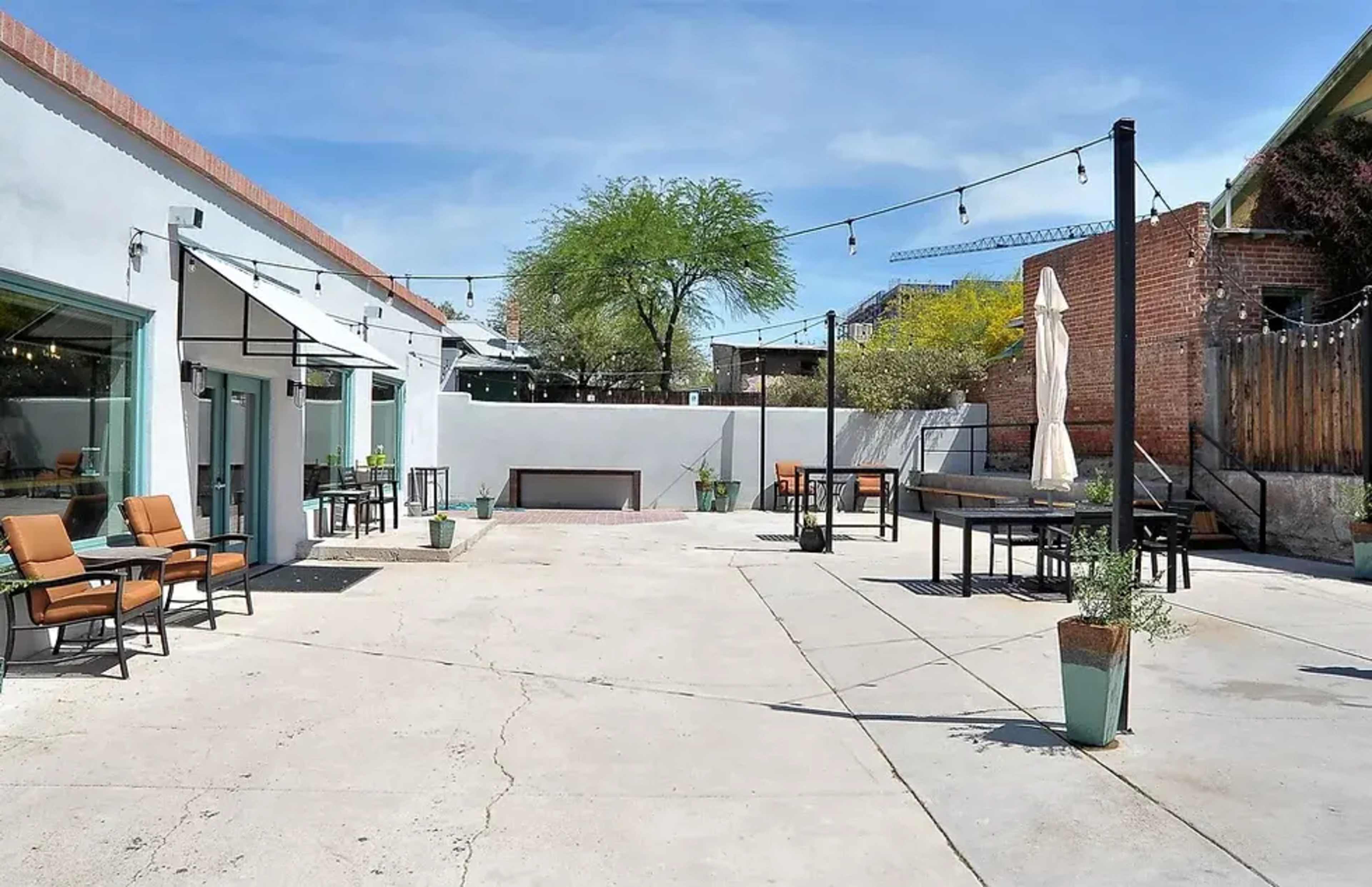 The image shows a spacious outdoor patio area with seating, planters, and string lights under a clear blue sky.