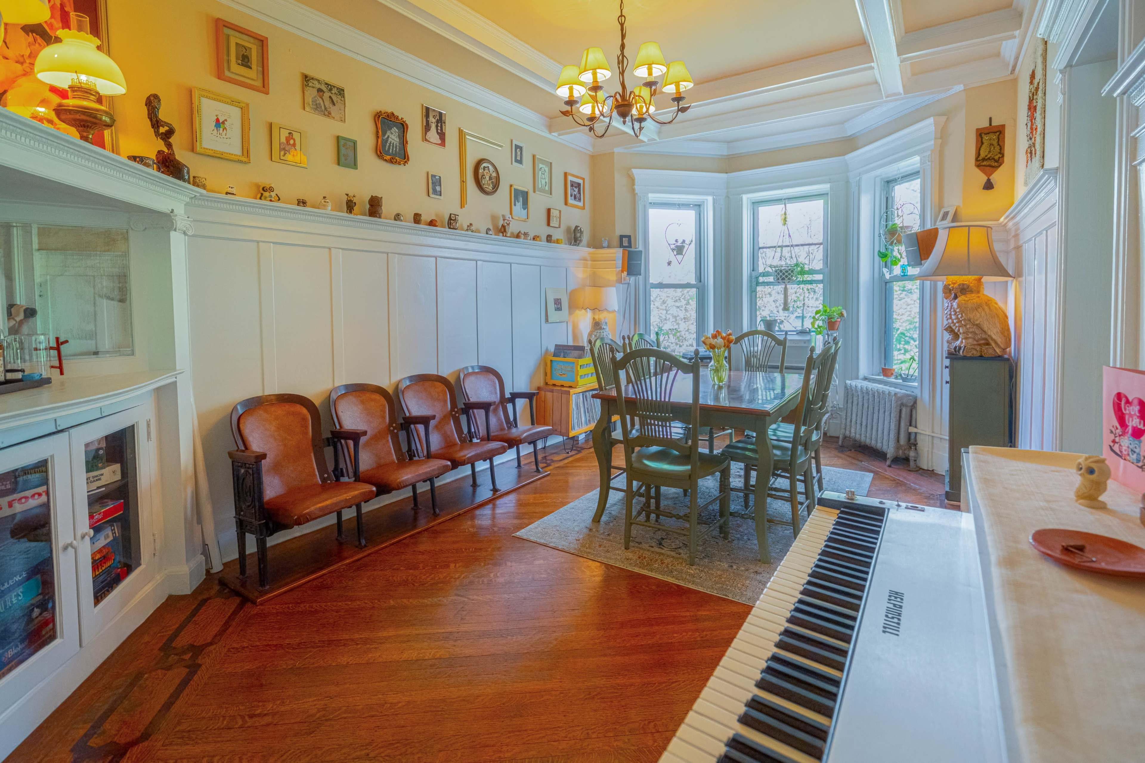 A cozy room features a dining table surrounded by chairs, with a row of vintage armchairs and walls adorned with framed pictures.